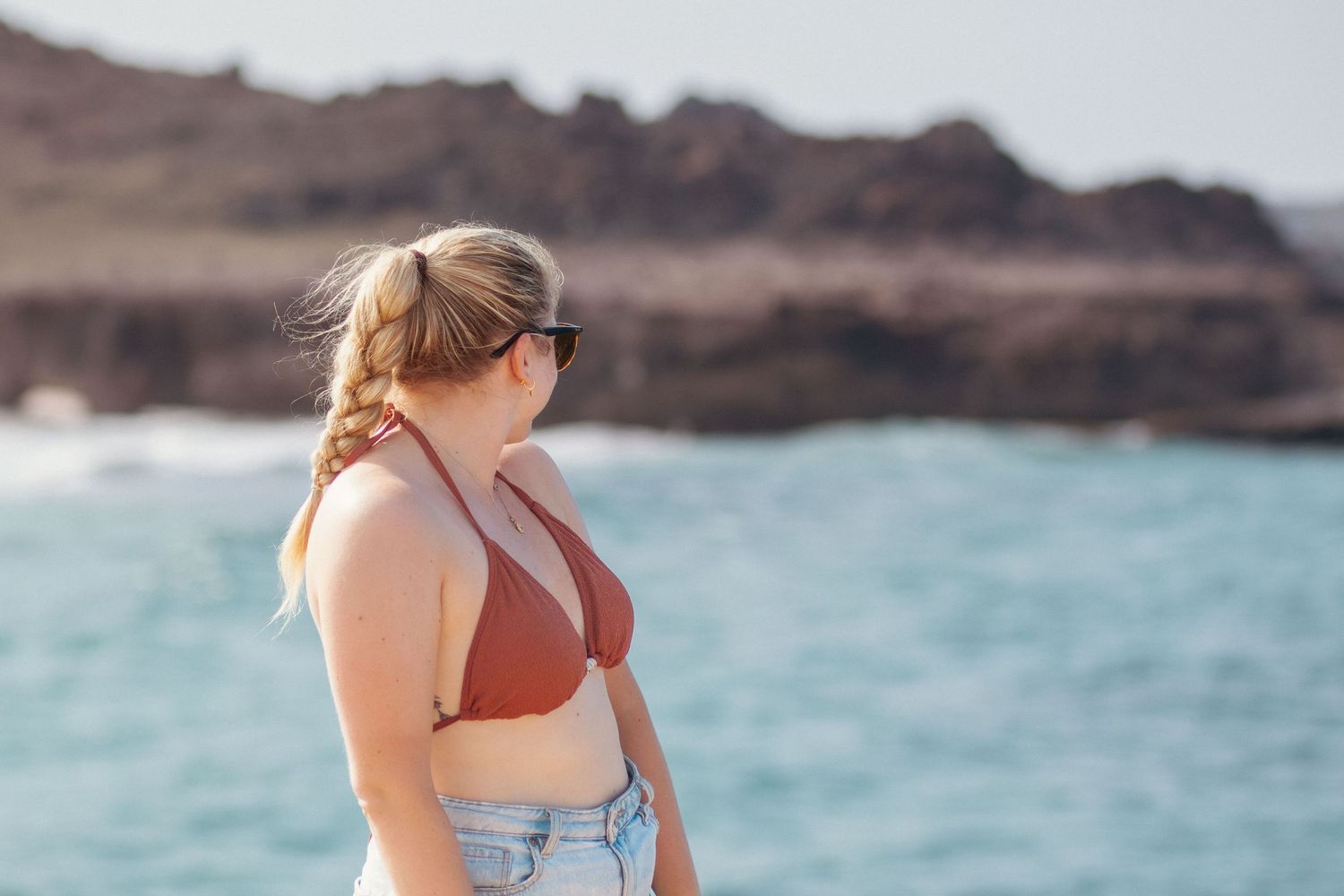 Series of people walking on a rocky coastal path overlooking turquoise waters and volcanic cliffs.