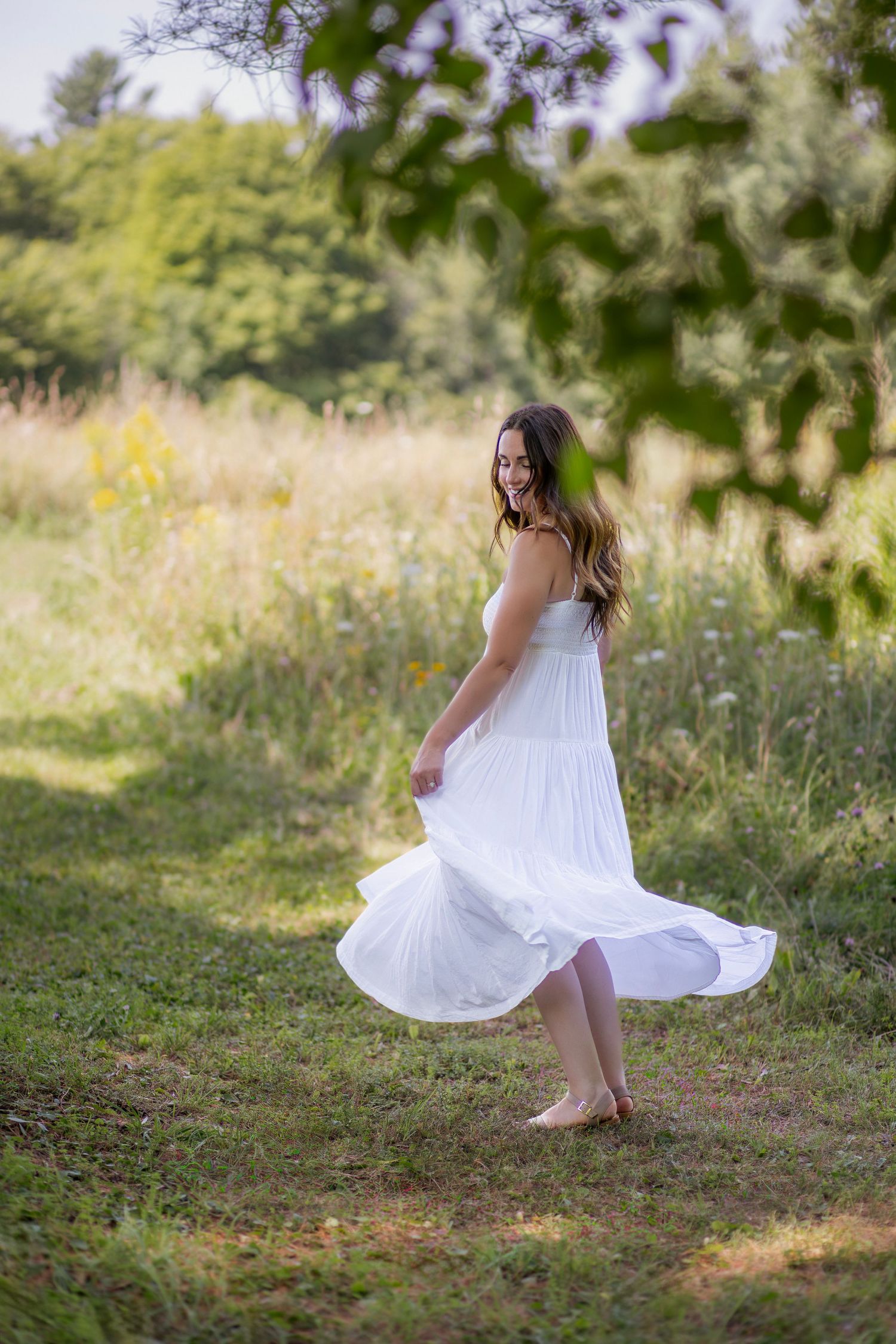 Woman in white sundress dances carefree in a summer meadow with wildflowers and trees.