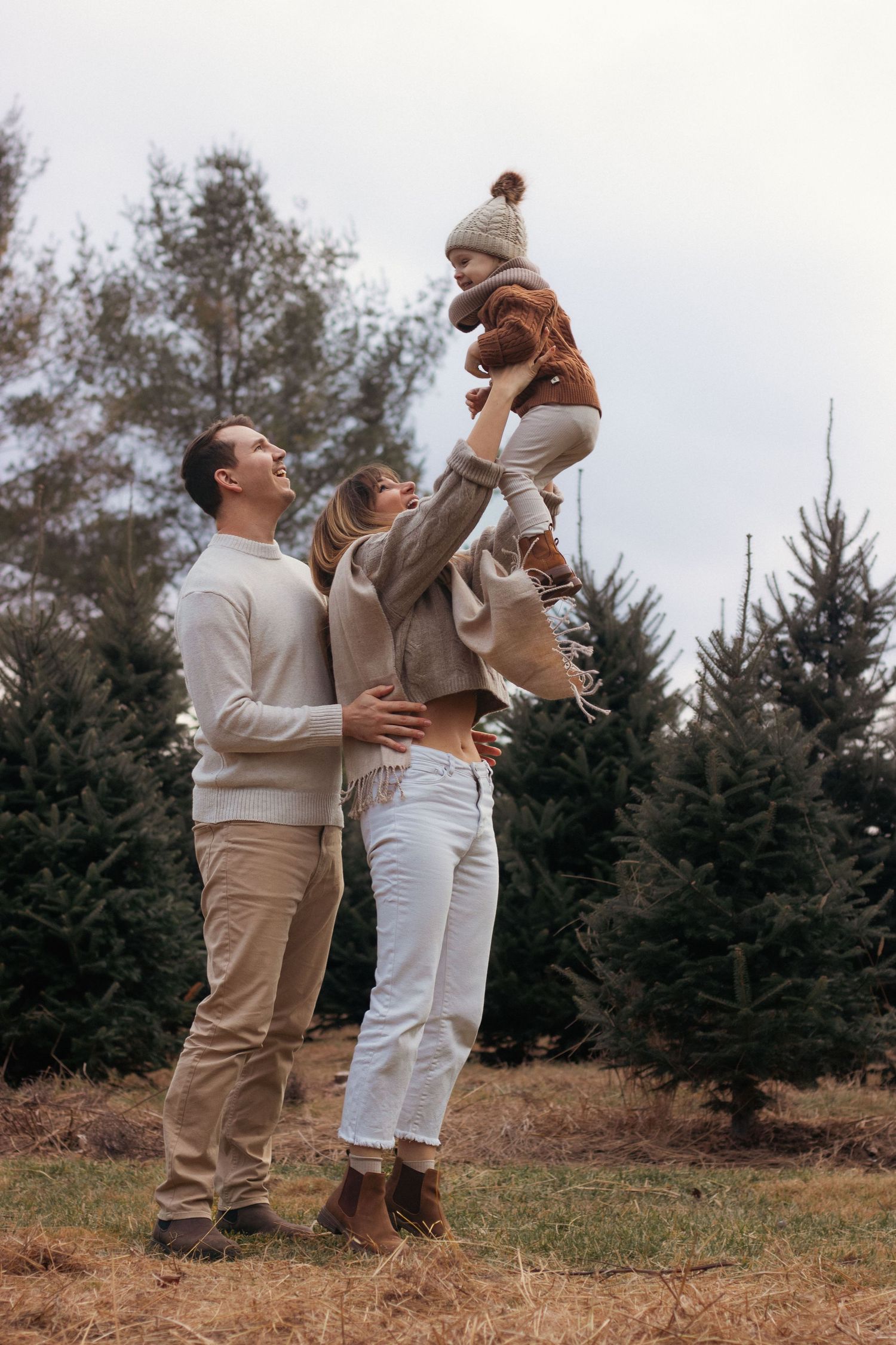 Playful family moment with child being lifted high in the air at a Christmas tree farm.