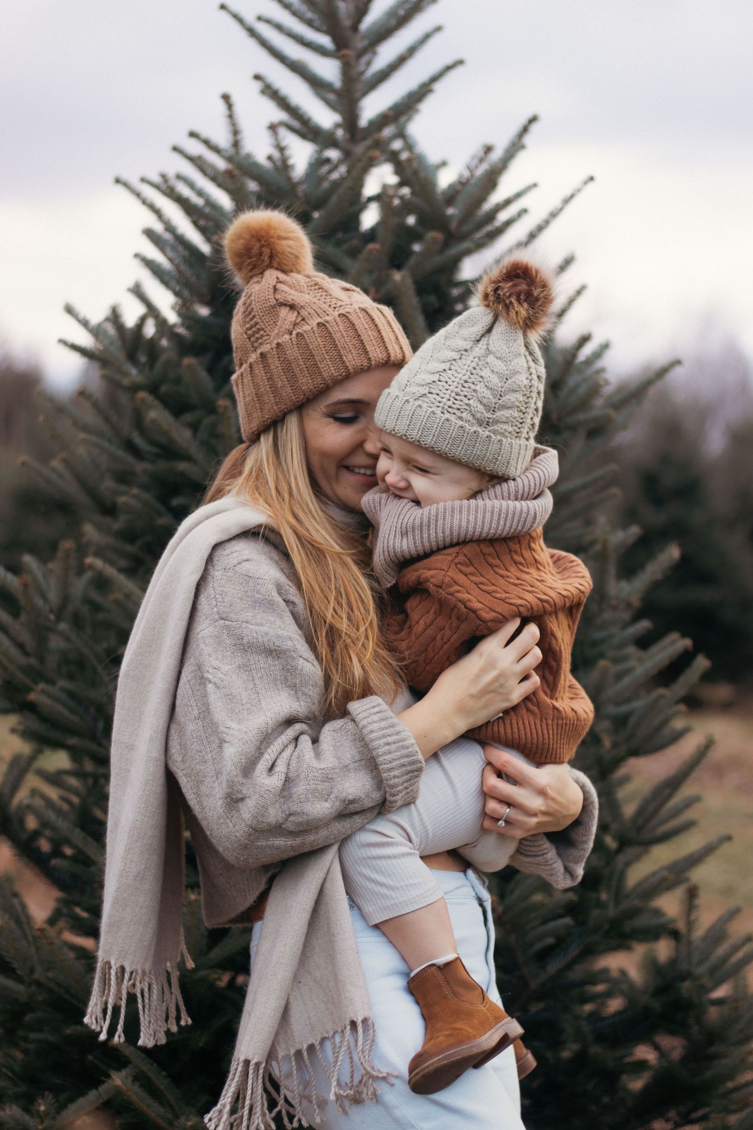 Cozy winter embrace with knit beanies and scarves against evergreen trees.