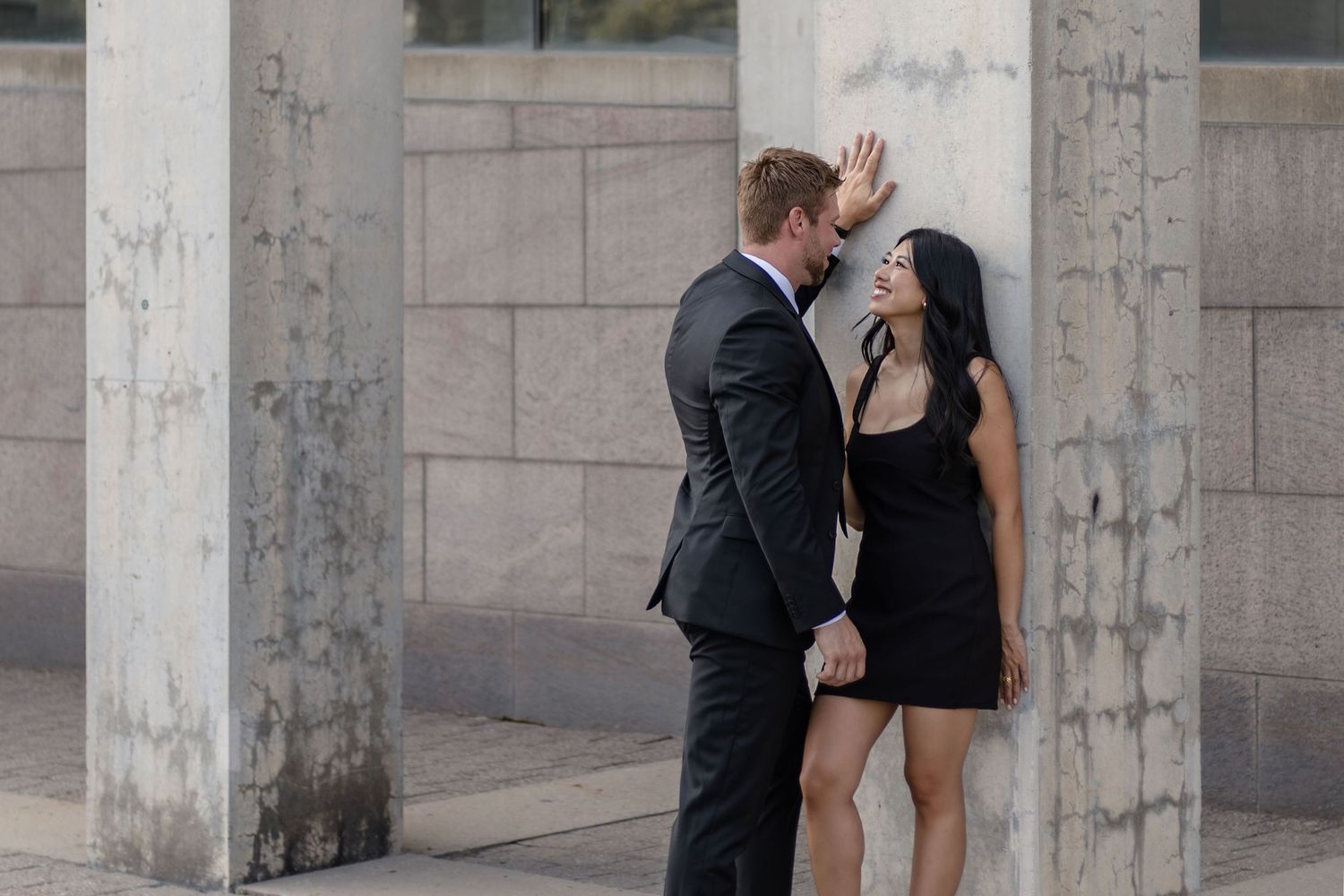 A couple shares an intimate dance together in a modern architectural space with concrete pillars.