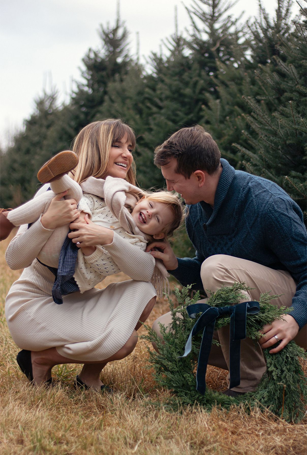Playful couple poses on grass near pine trees during outdoor photoshoot.
