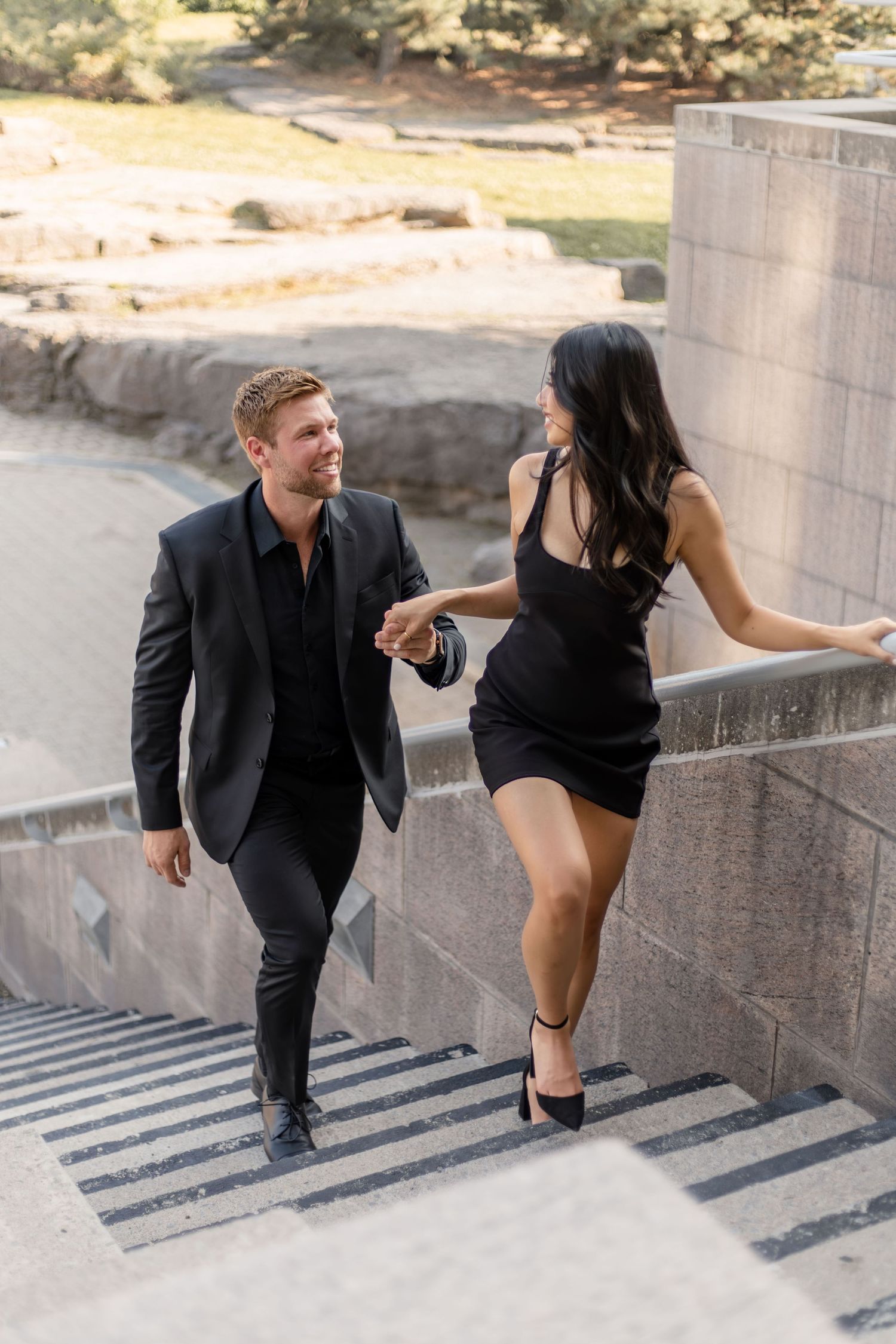Couple in formal wear playfully climbing concrete stairs outdoors.