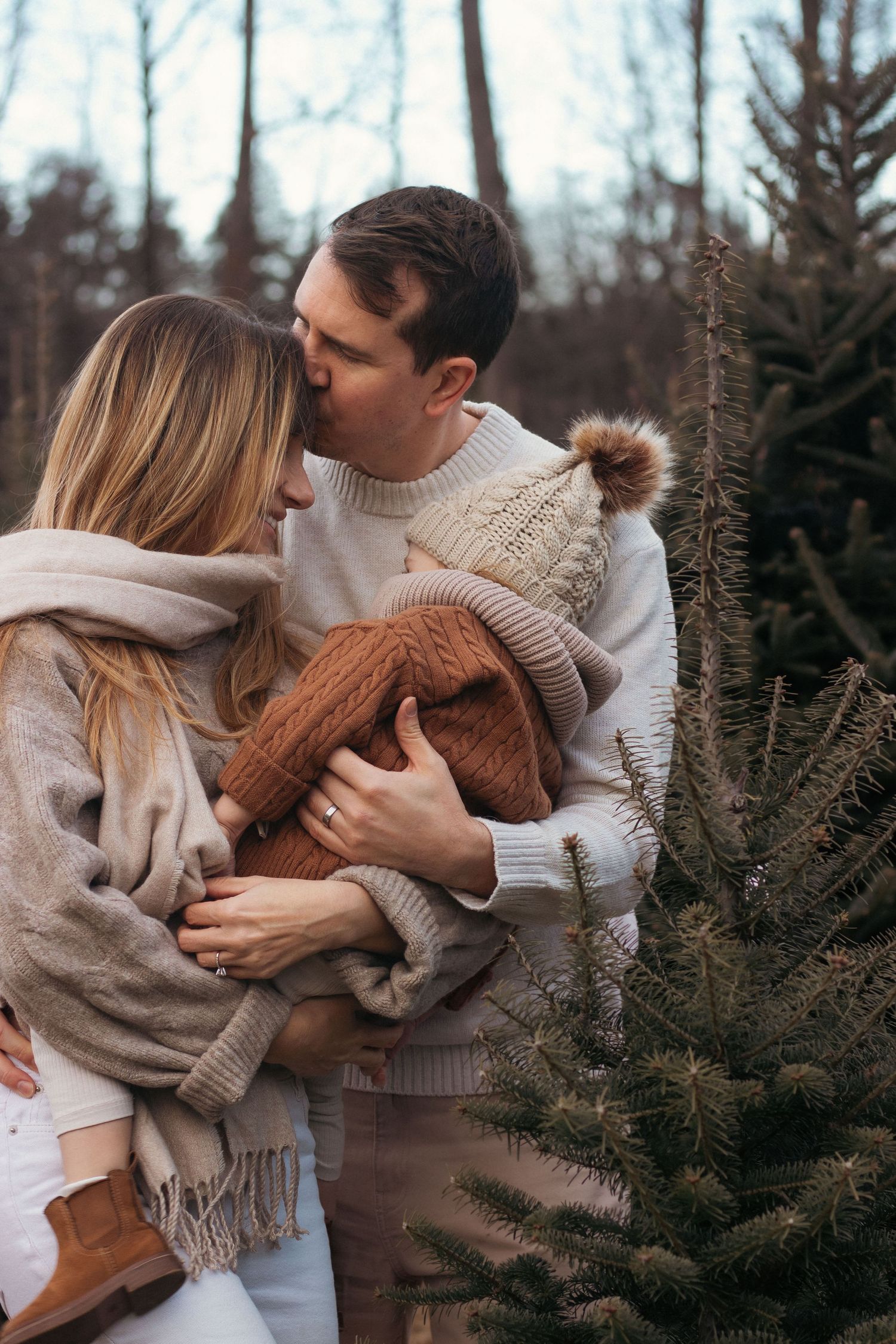 Intimate outdoor photoshoot near evergreen trees with people wearing neutral winter clothing.