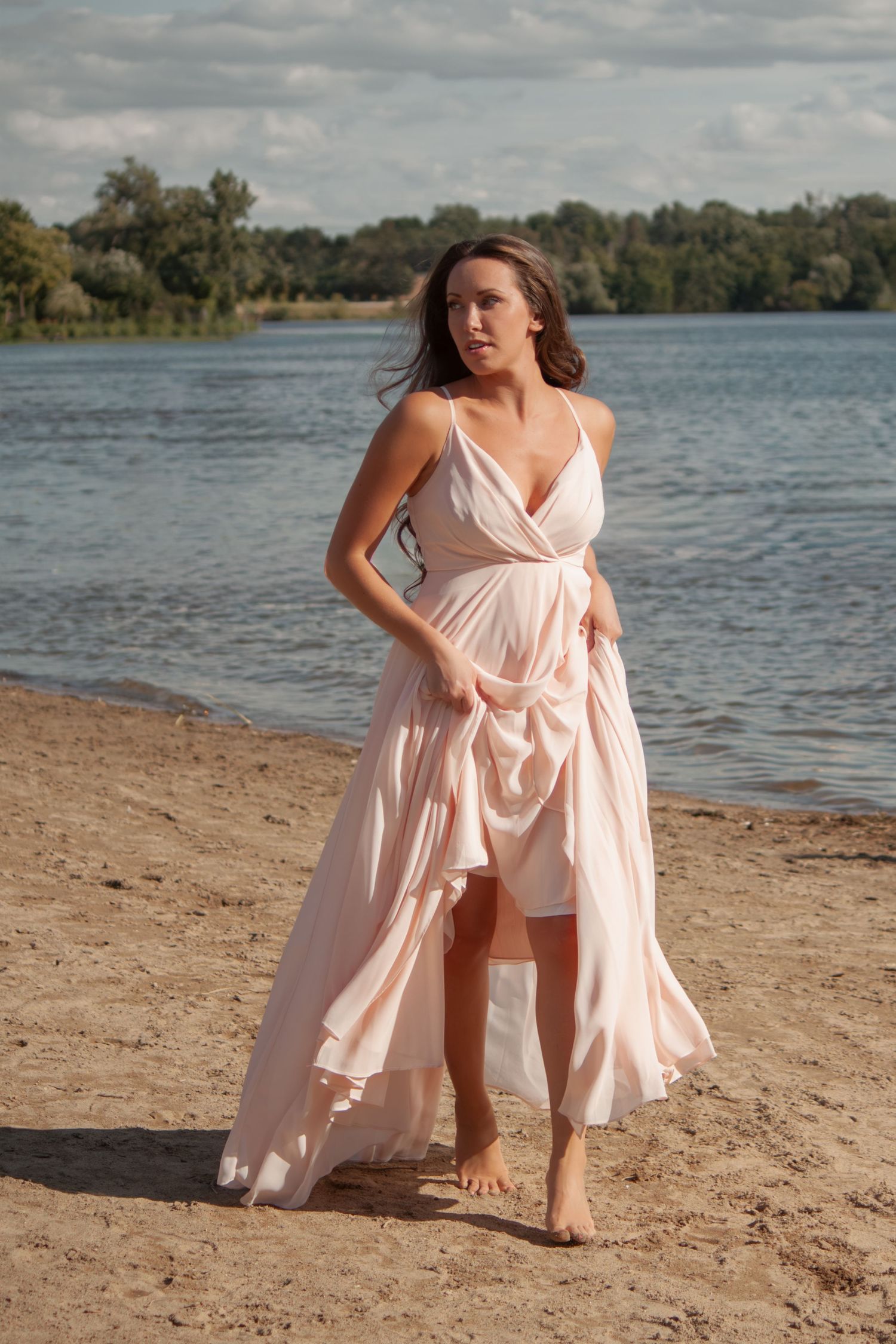 A romantic beach photoshoot featuring a flowing pink dress against a lakeside backdrop.
