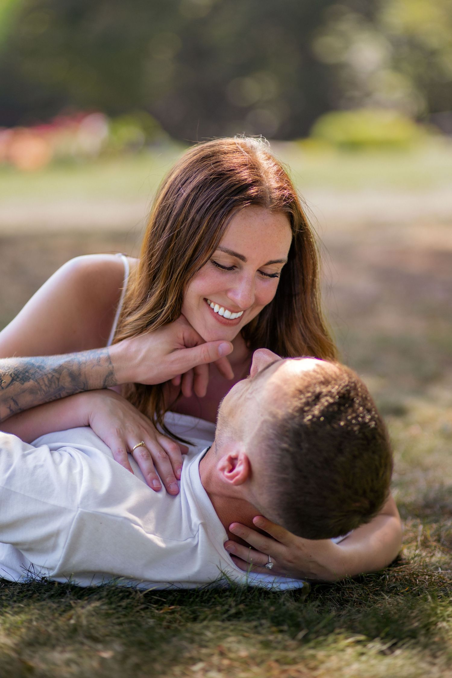 Intimate couple moment captured on grass with soft natural lighting and white attire.