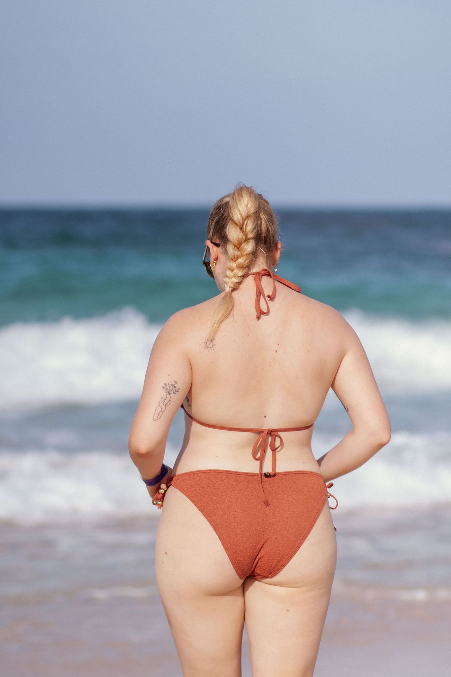Person in orange swimwear walking along beach with ocean waves in background.