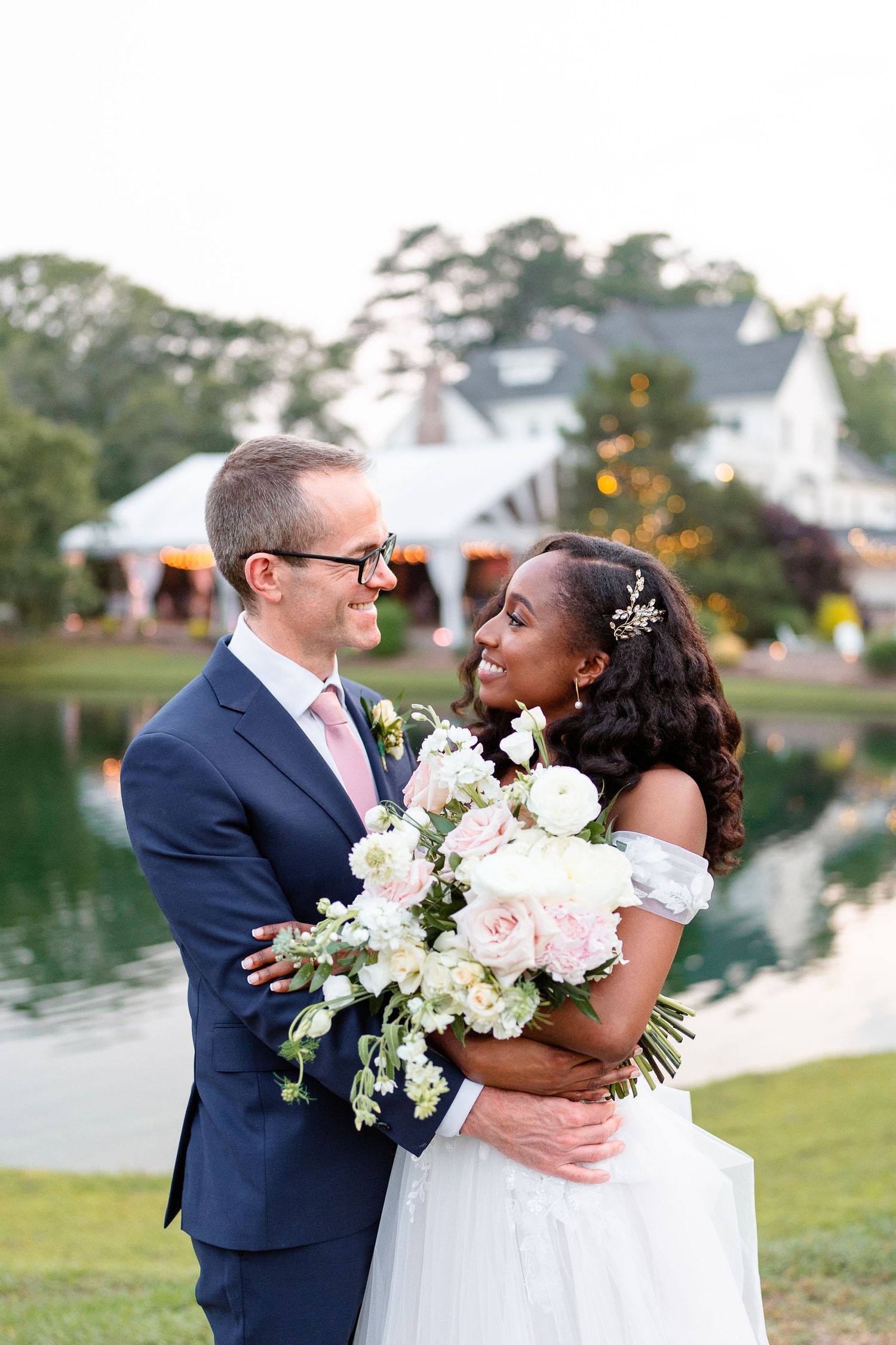 Newlyweds share intimate moment by lakeside venue with white floral bouquet.