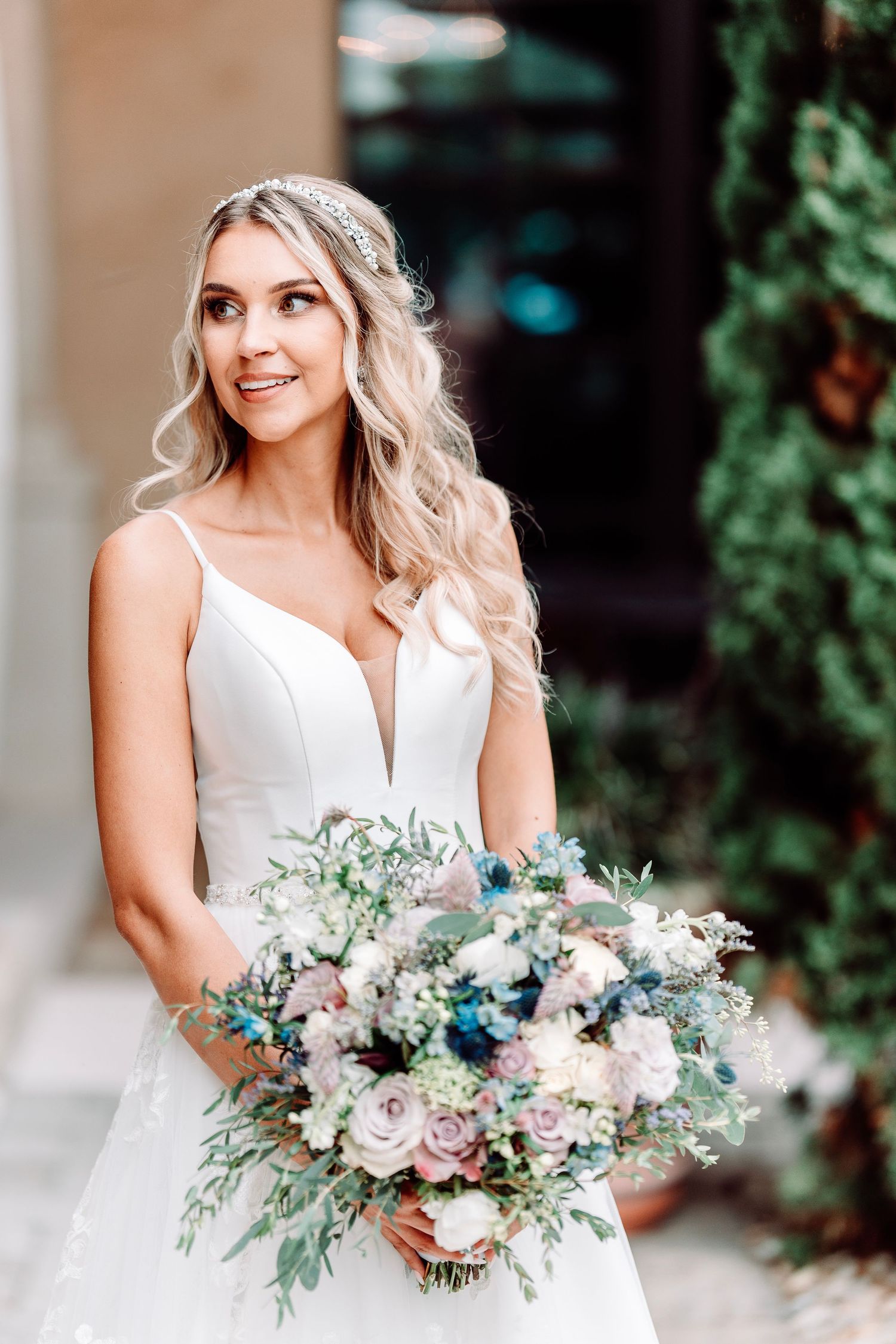 Bride holds pastel bouquet with eucalyptus in classic white v-neck wedding gown.