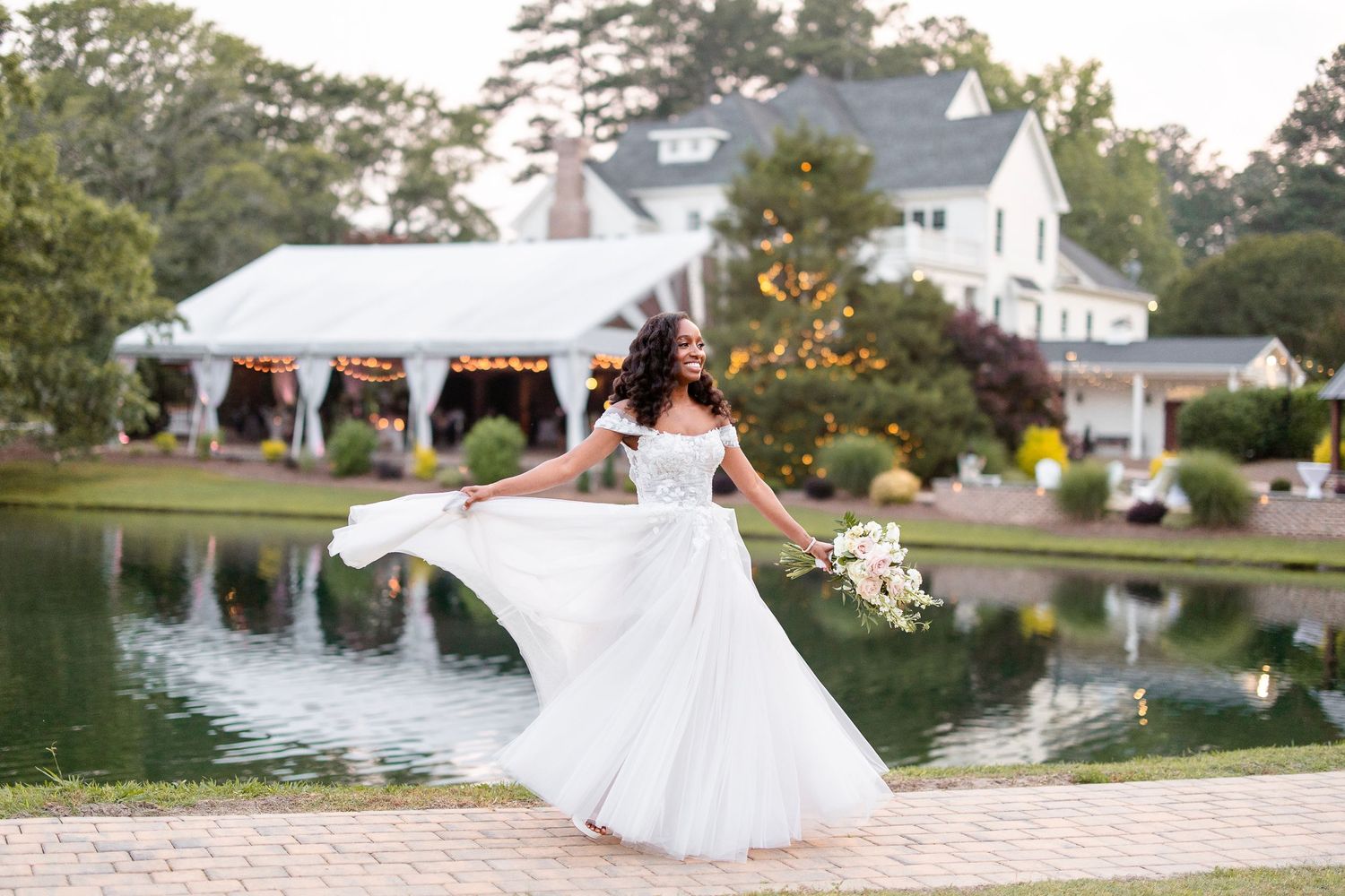 Flowing white wedding dress twirling on brick patio by lakeside venue.