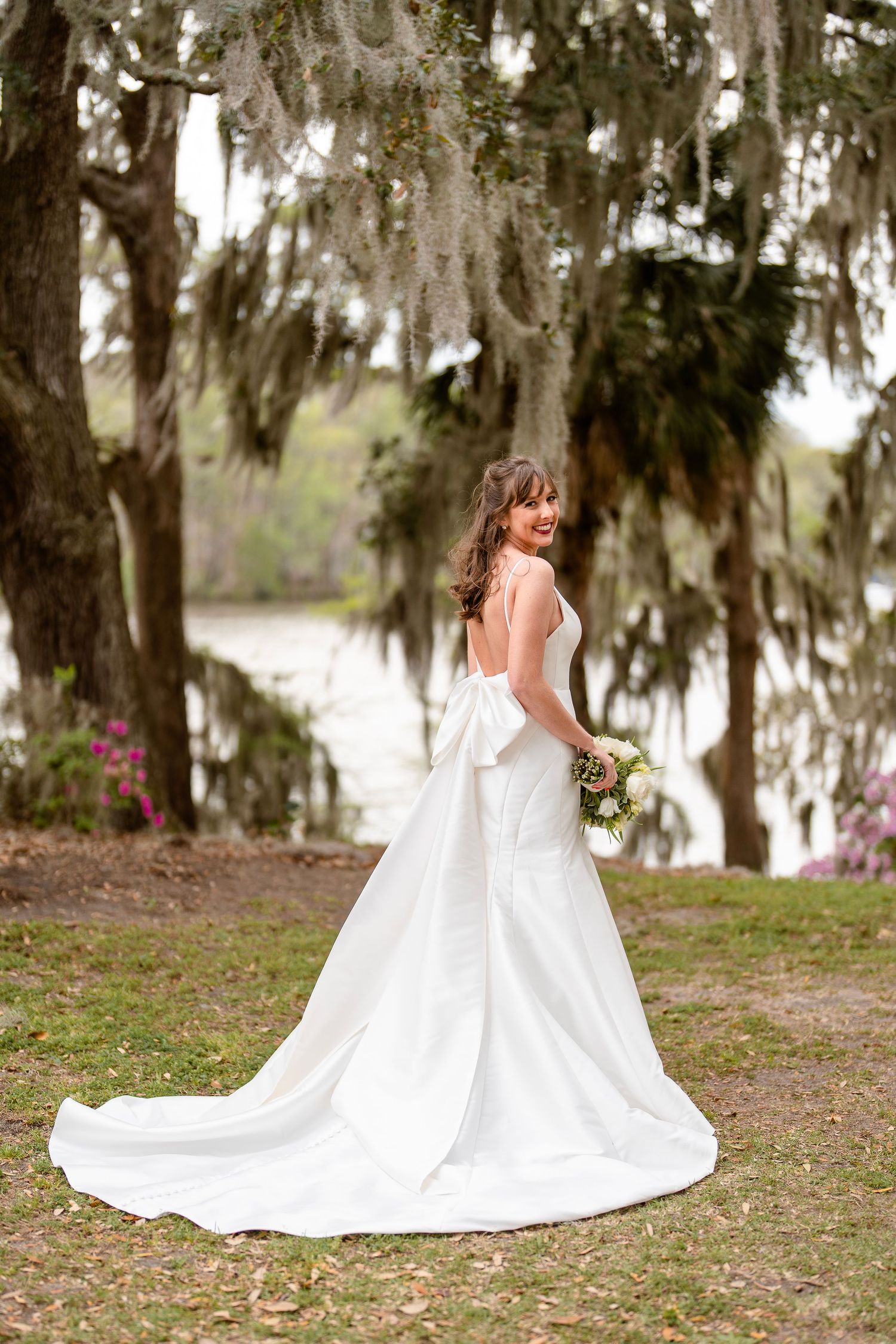 Elegant bridal portrait in a flowing white gown among Spanish moss-draped trees.