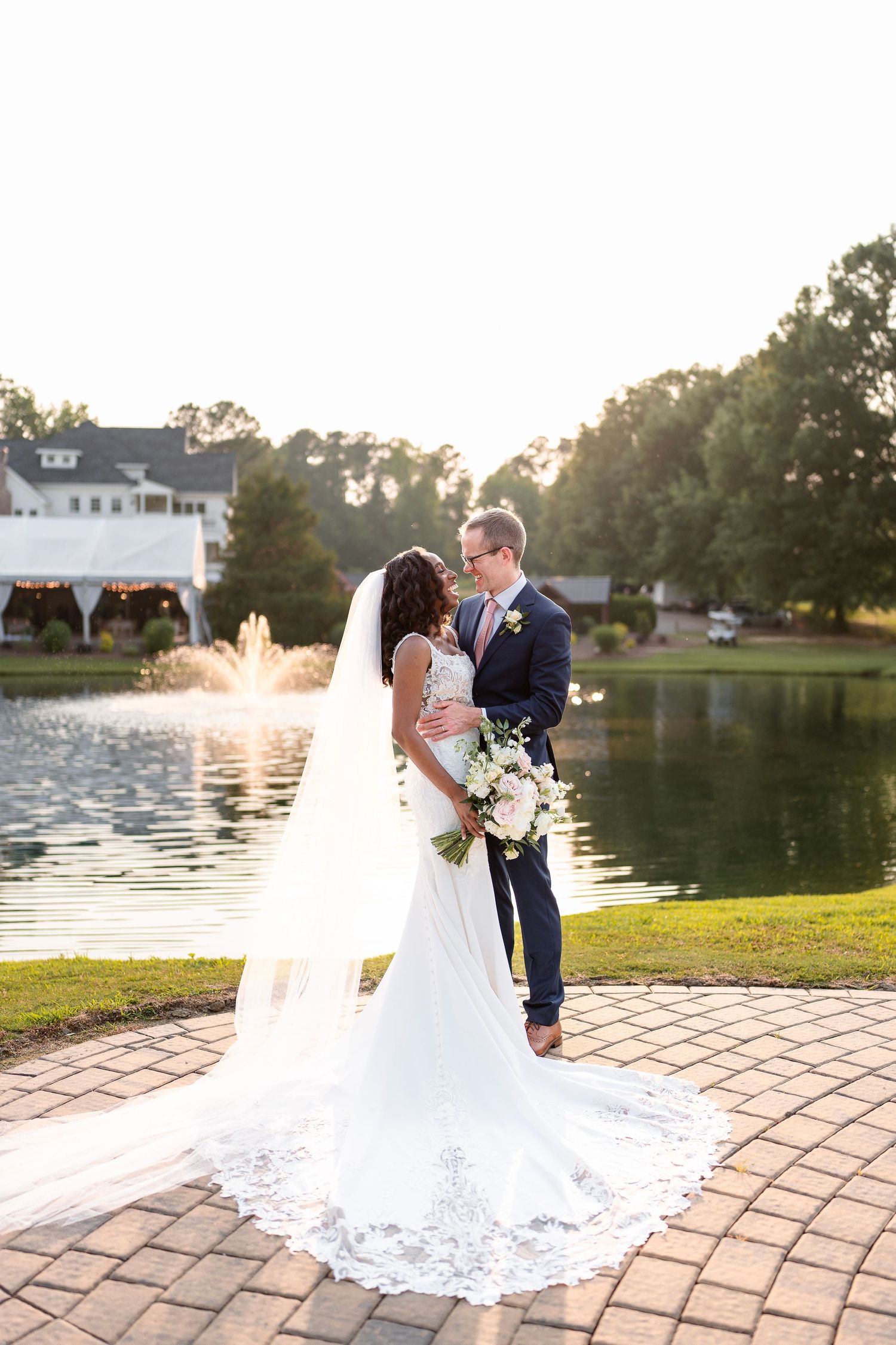 Romantic sunset wedding portrait by lakeside with white house in background.