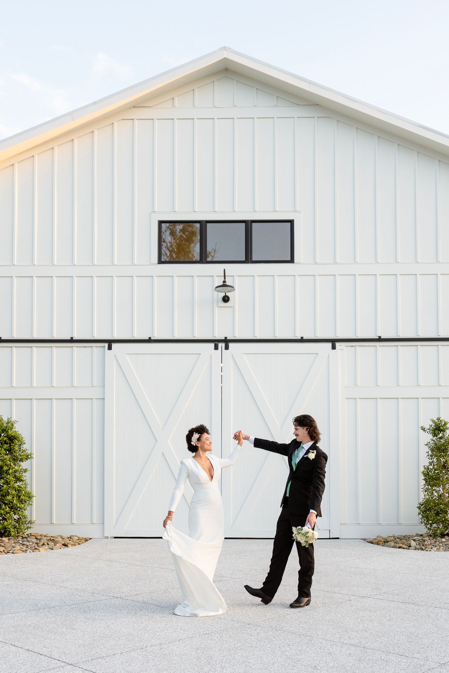 A romantic dance moment between a couple in formal attire in front of a white barn.