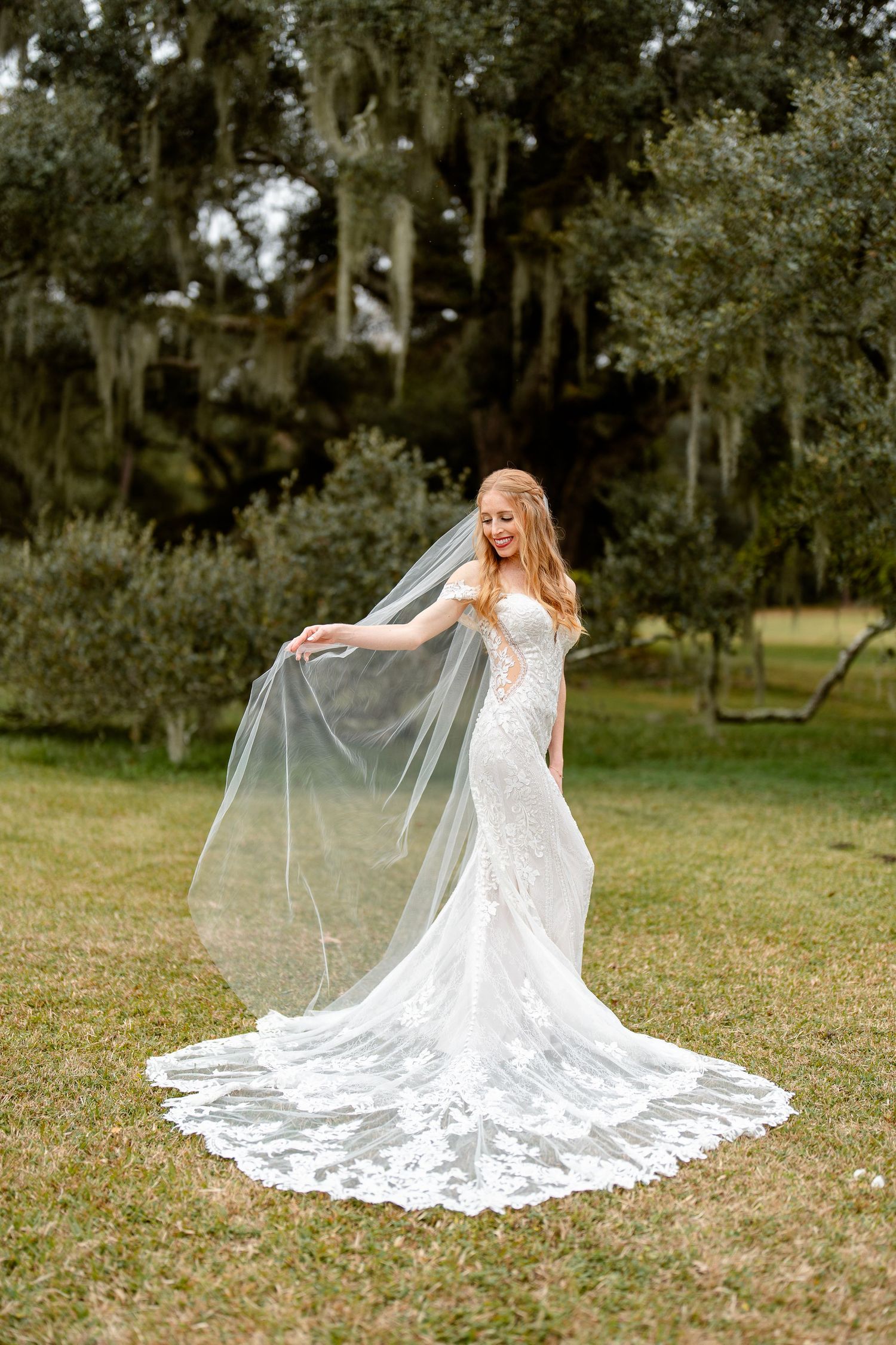 Bride twirls in fitted lace wedding dress with dramatic cathedral train outdoors.
