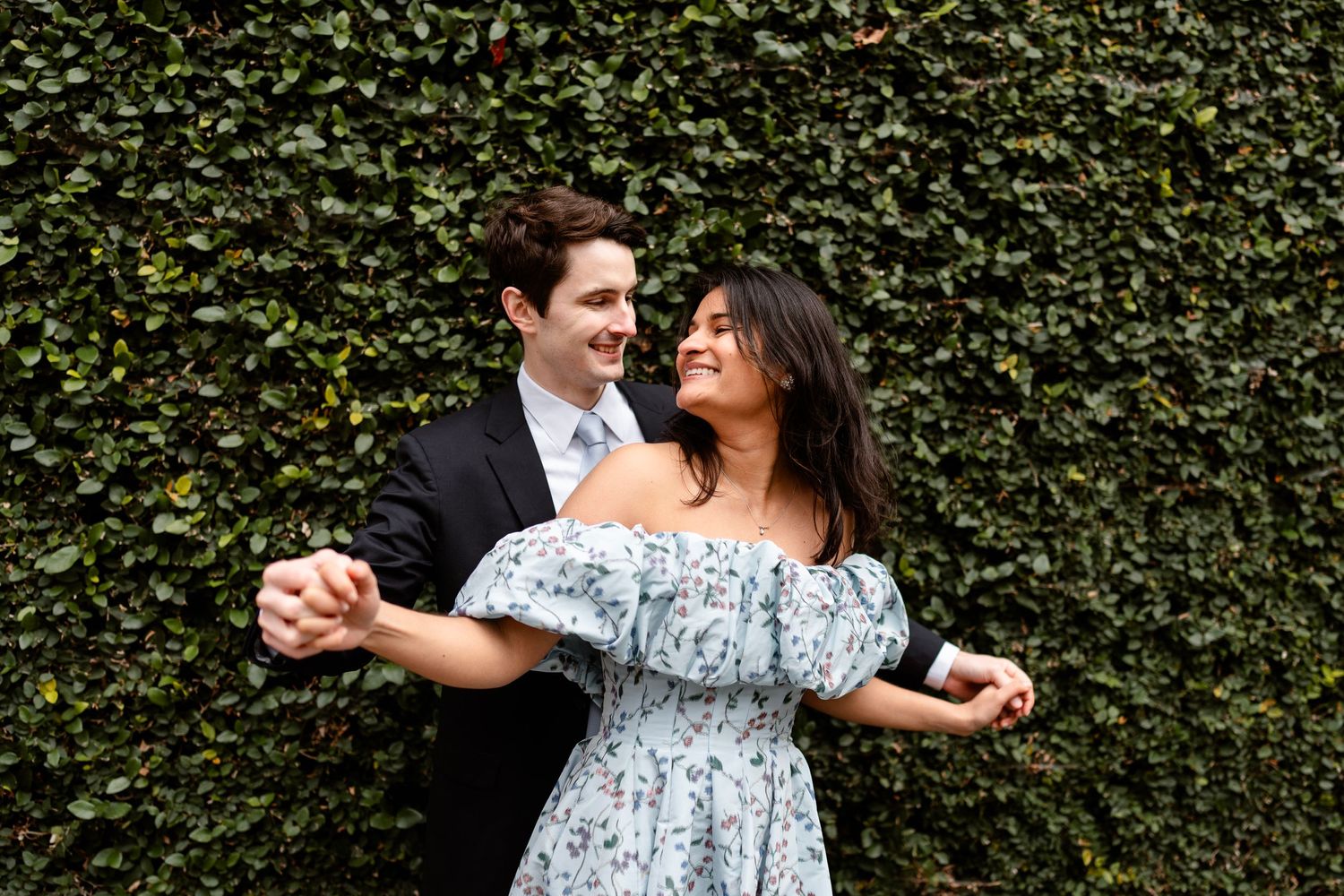 A couple dances playfully against a backdrop of lush green ivy.
