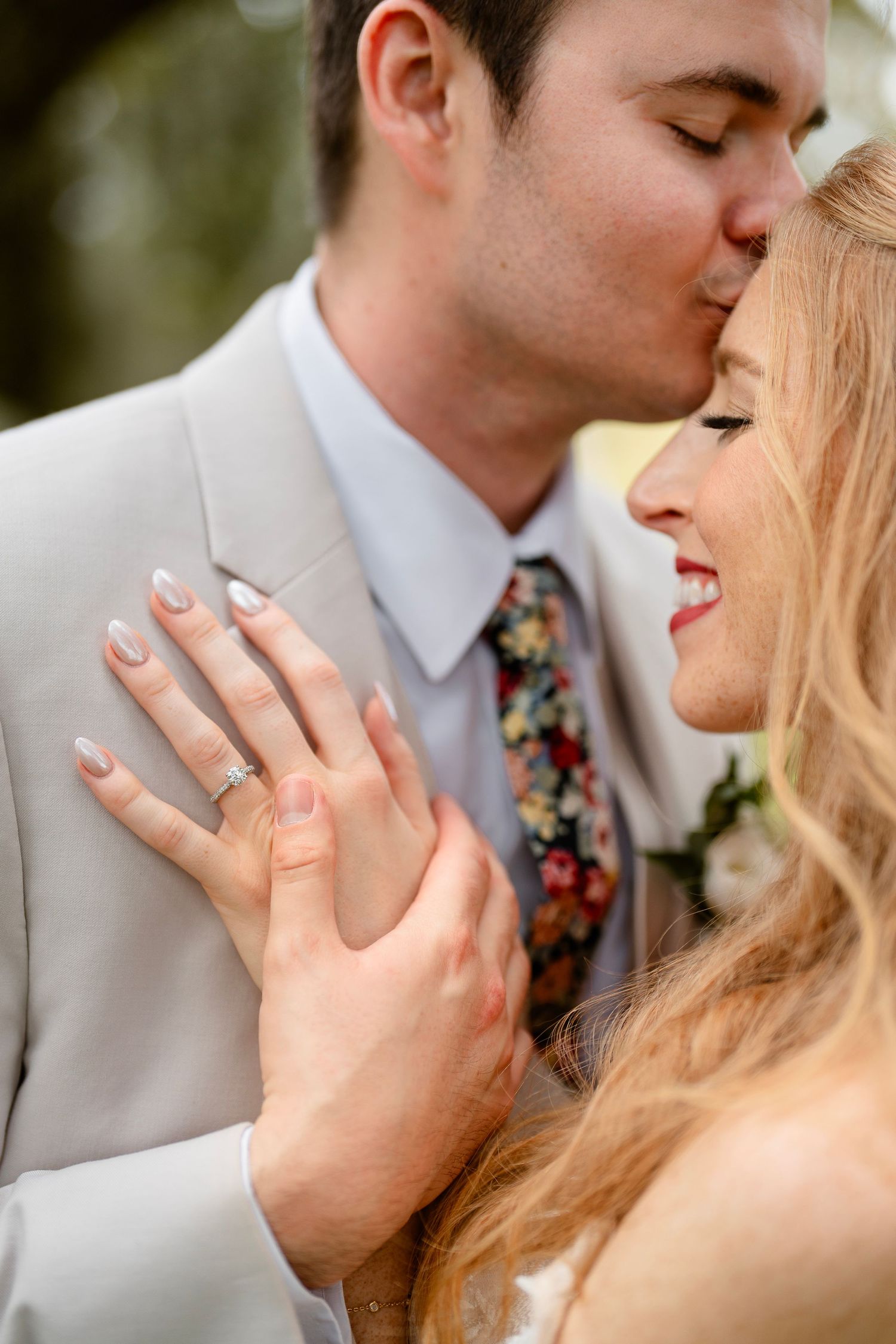 Close-up of intimate wedding moment showing engagement ring and floral tie.