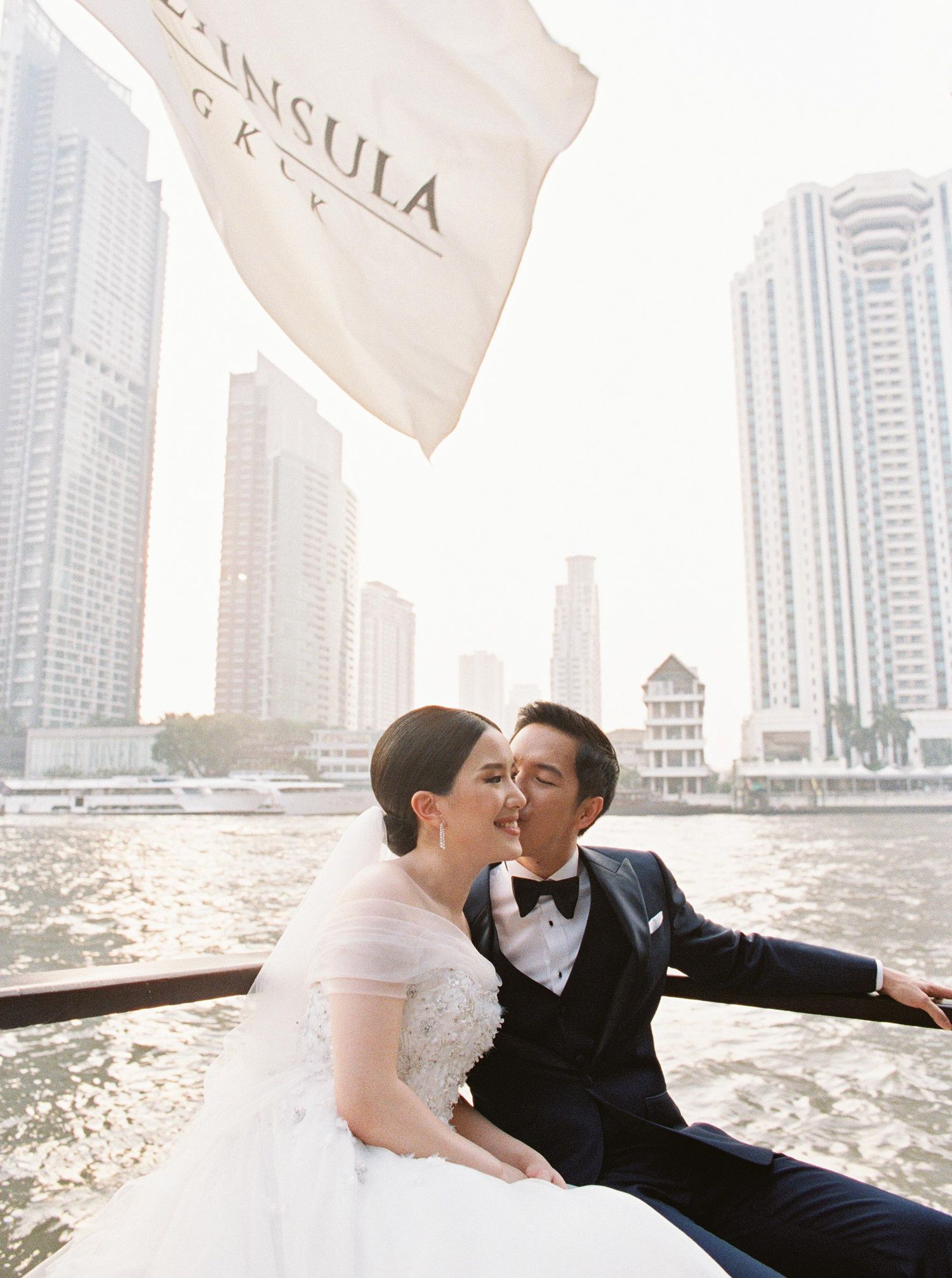 Elegant wedding moment at The Peninsula Bangkok, Thailand, featuring a romantic couple with a stunning riverside city vi