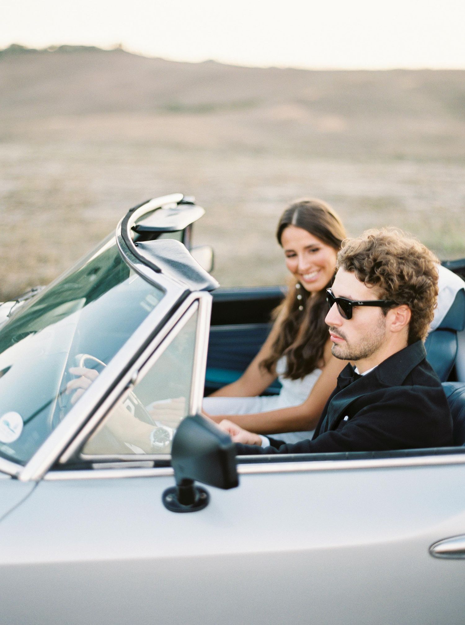 Stylish wedding couple driving a vintage car in scenic Baccoleno area, Tuscany, Italy, capturing elegance and romance.