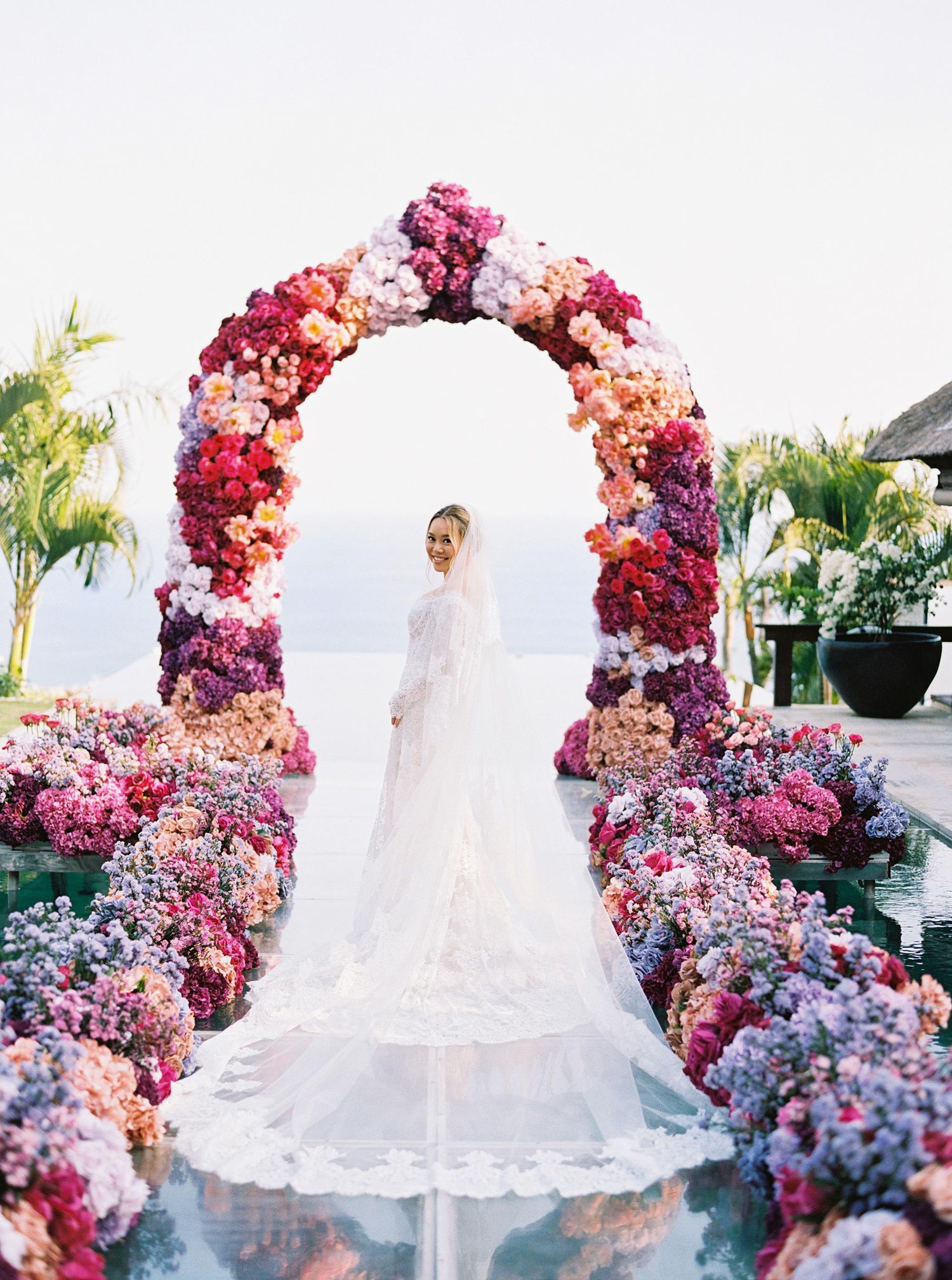 Stunning bride at Bulgari Resort Bali under a vibrant floral arch with ocean views, showcasing luxurious wedding eleganc