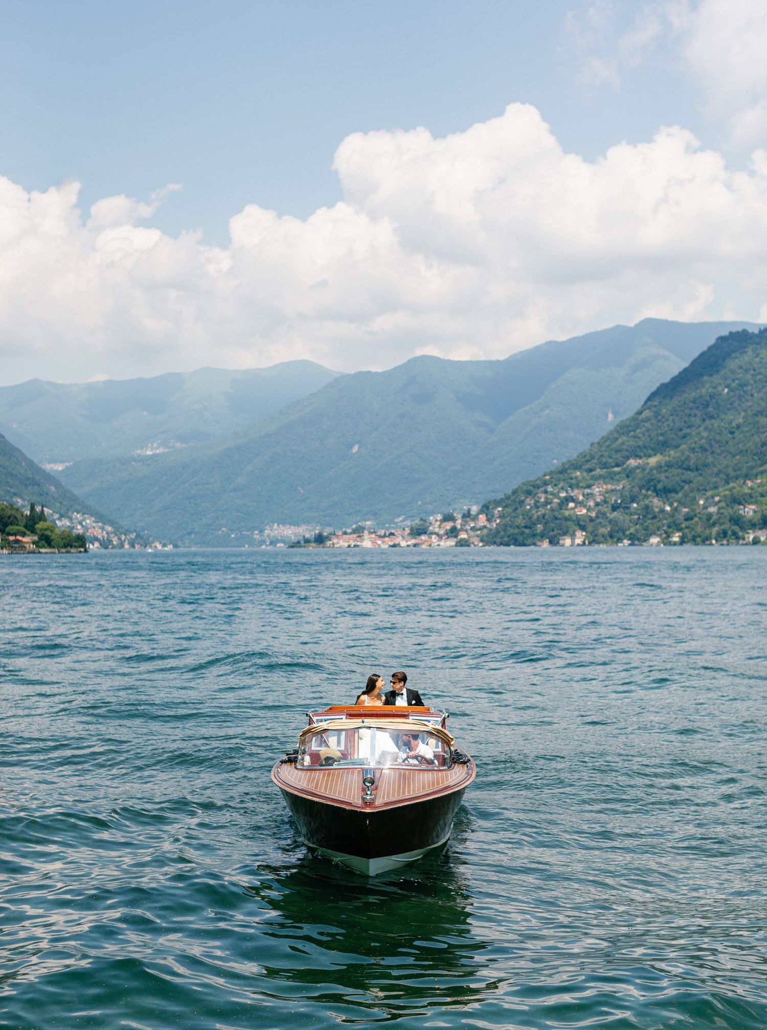 Elegant wedding couple on a boat at Lake Como, Italy, with scenic mountain views, perfect for the Villa Erba gallery.