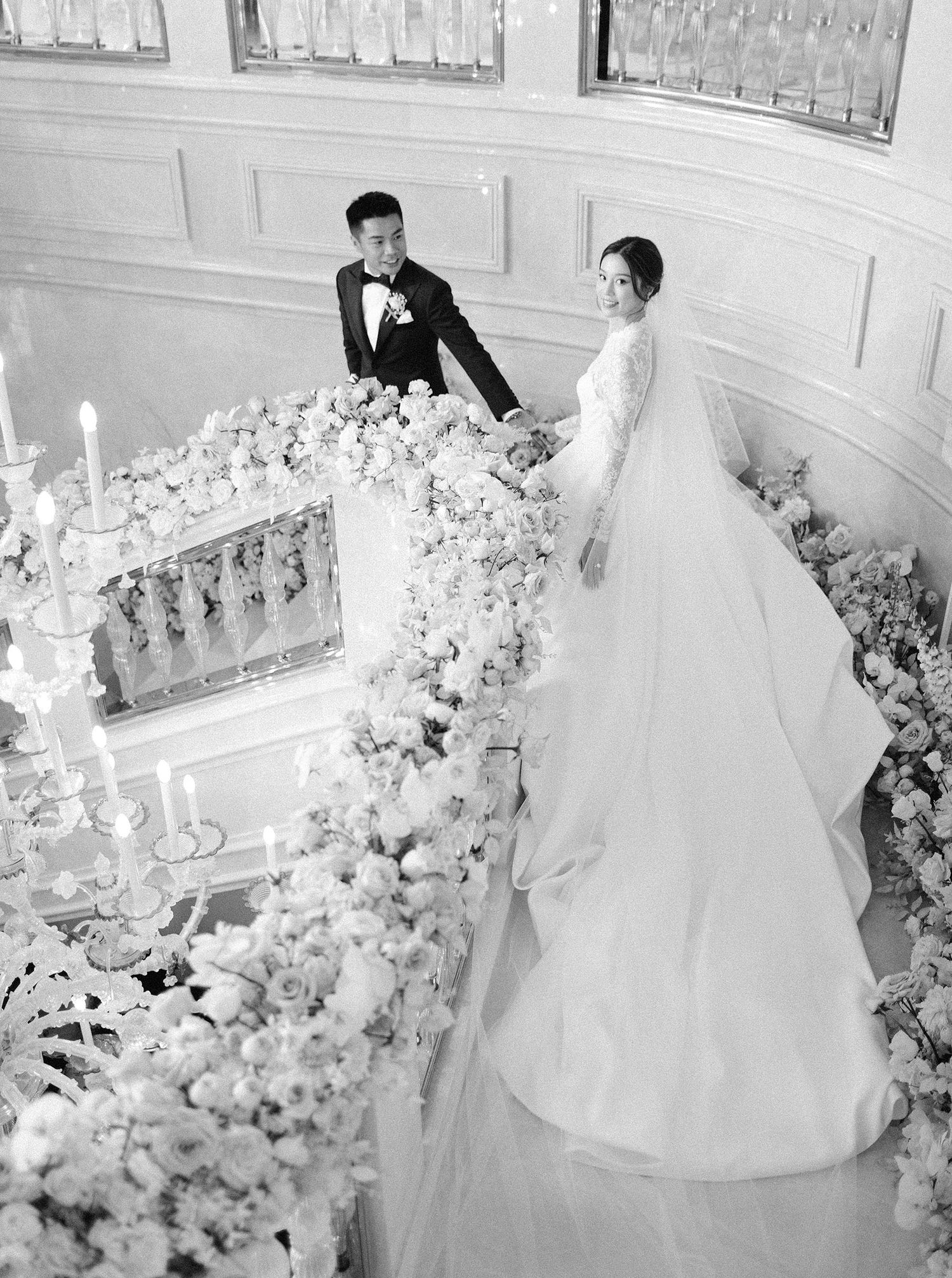 Elegant wedding couple in Hong Kong on a floral-adorned staircase, featuring a luxurious gown and sophisticated details.