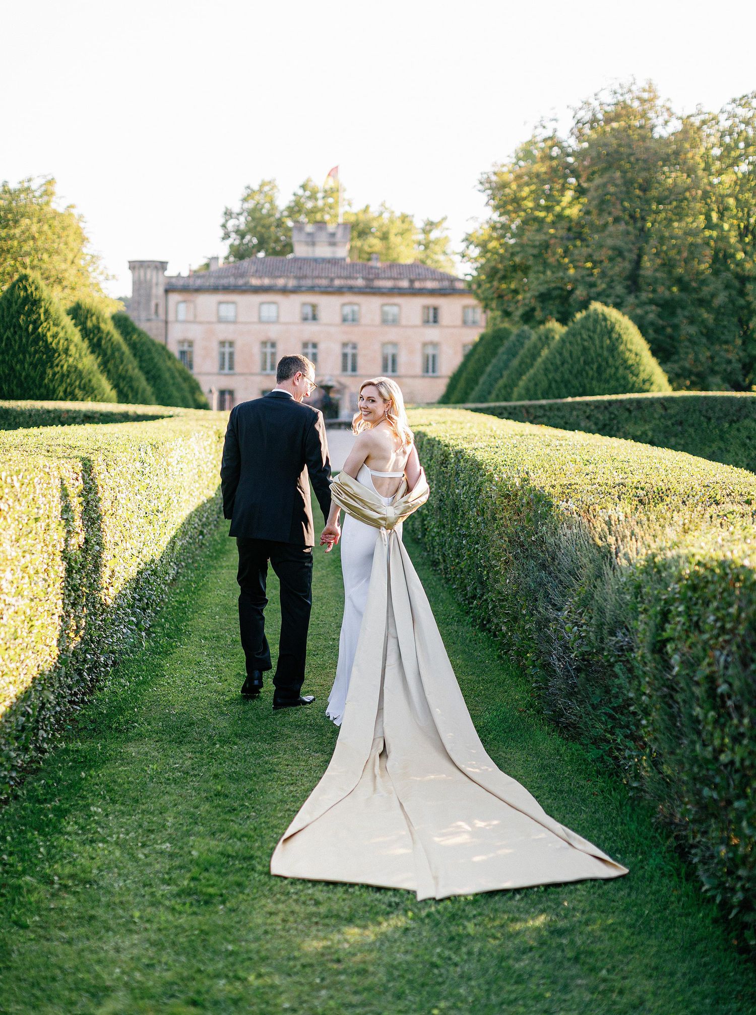 Couple walking through a manicured garden hedge maze at an elegant estate during sunset.