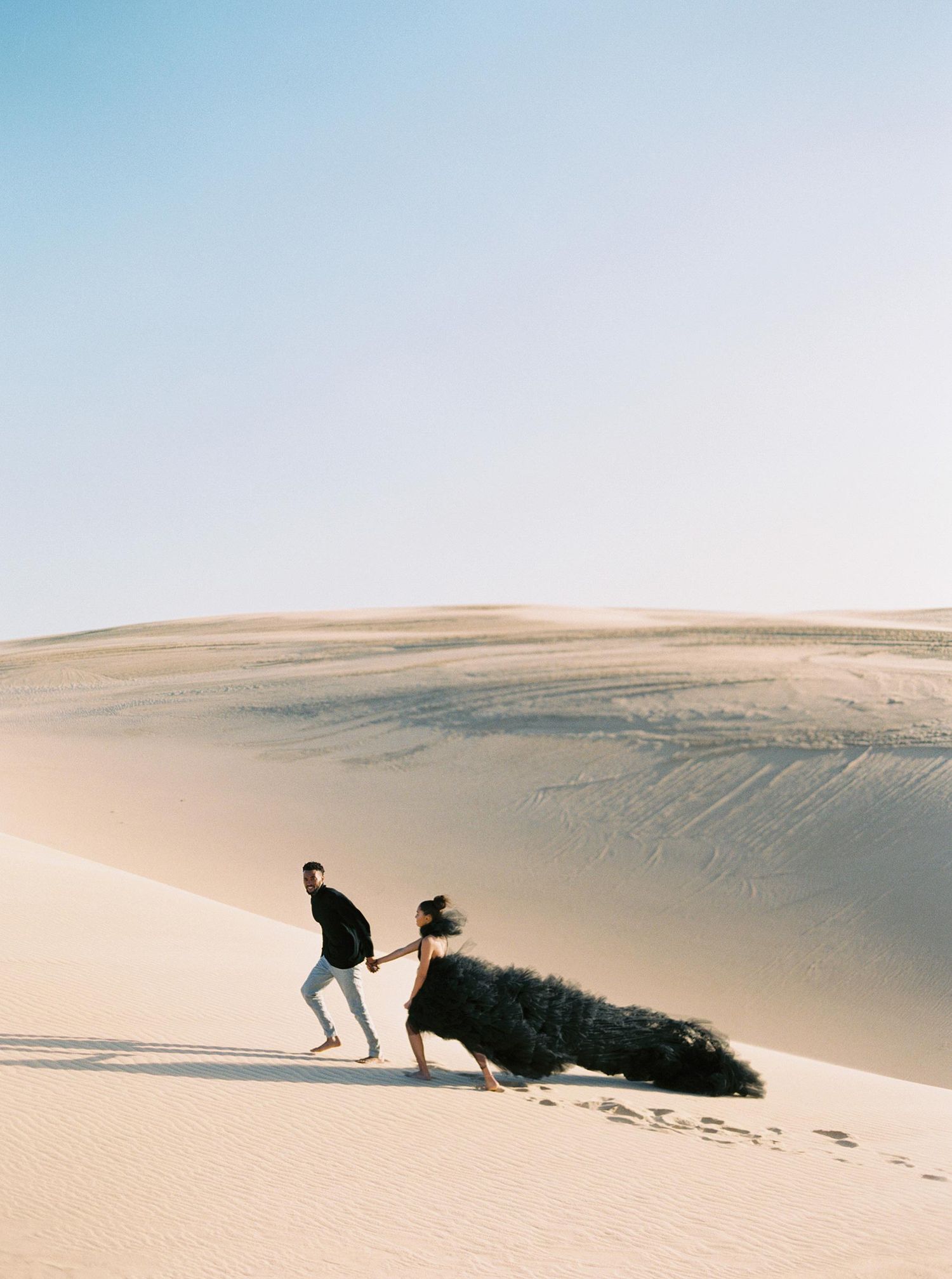 Wedding couple in Mozambique, Africa, walking on sand dunes with dramatic scenery and a flowing gown.