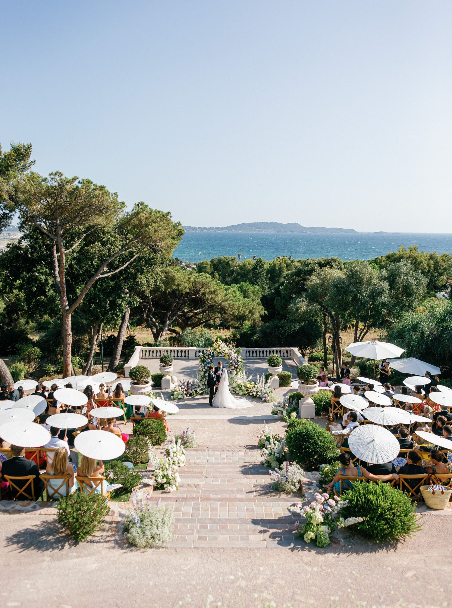 Elegant outdoor wedding ceremony with white sun umbrellas overlooking a Mediterranean sea at French Riviera.
