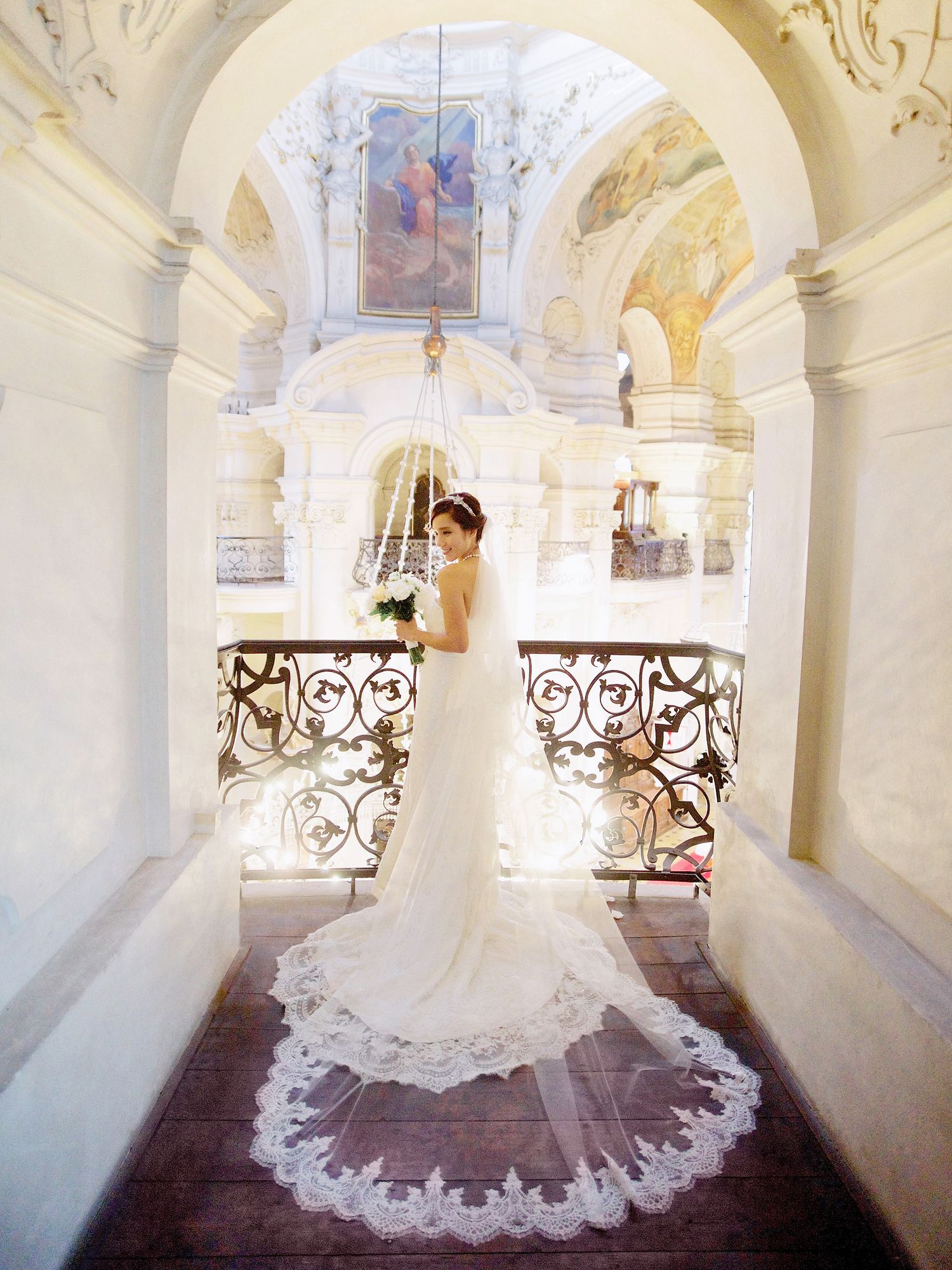 Best wedding photographer in Prague captures an elegant bride with long veil posing in church.