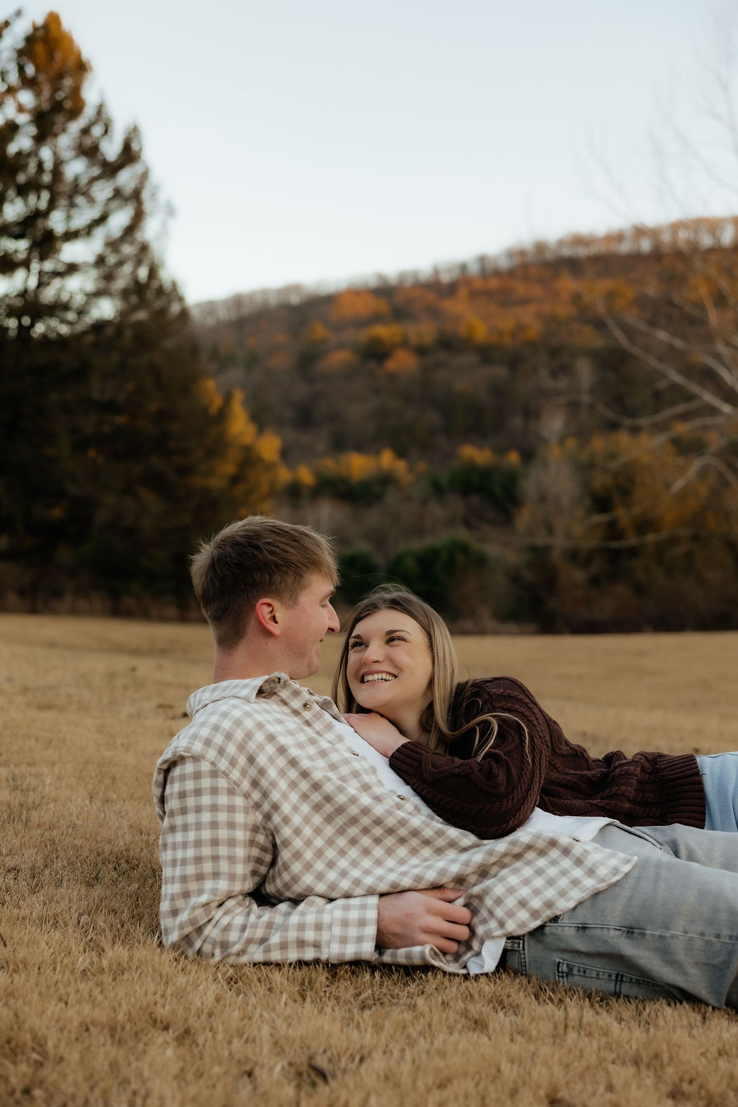 A couple lying together in a golden autumn field during sunset, sharing an intimate moment in nature.