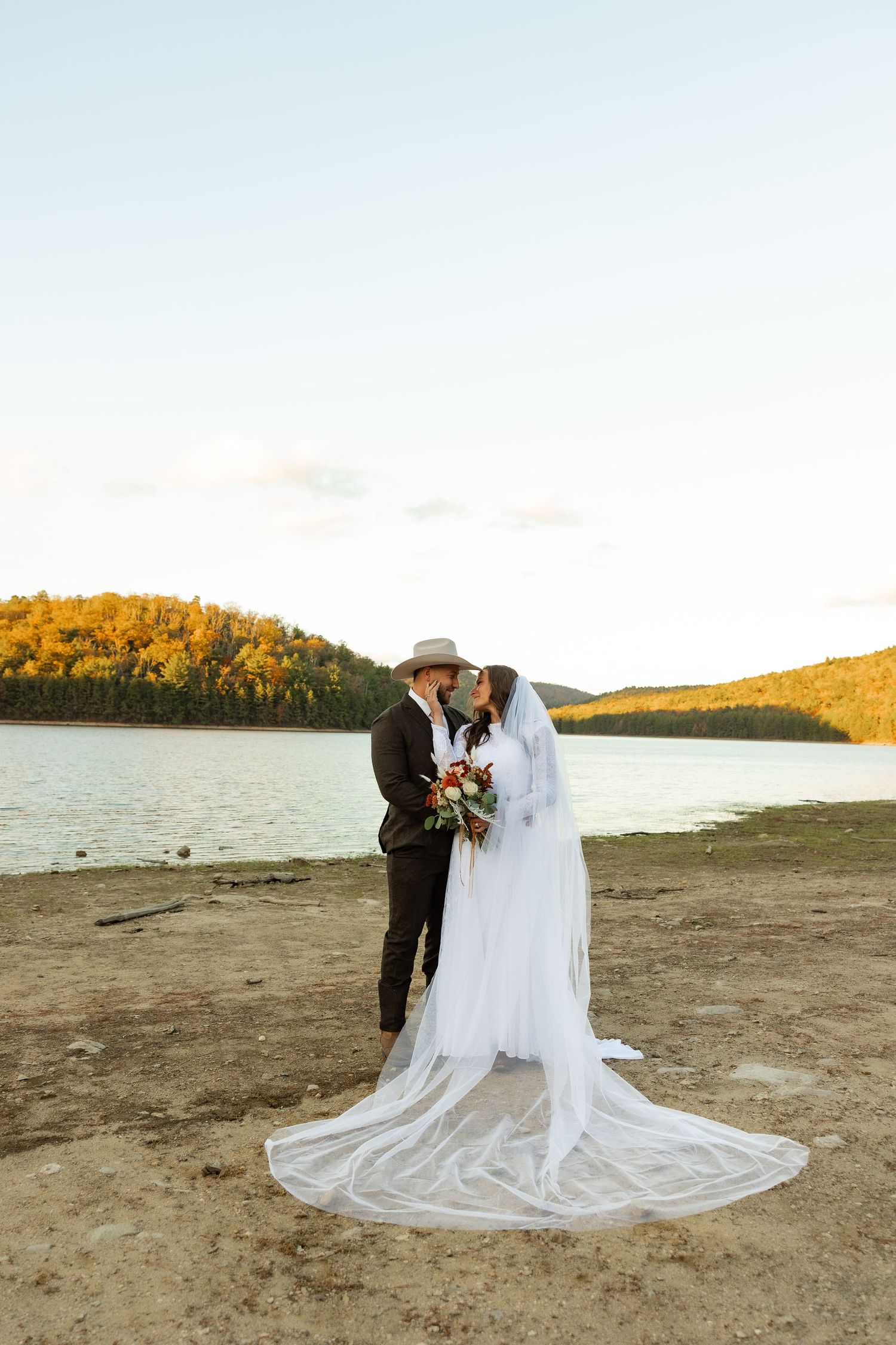 A romantic beach wedding photoshoot with a flowing white dress and scenic autumn backdrop.