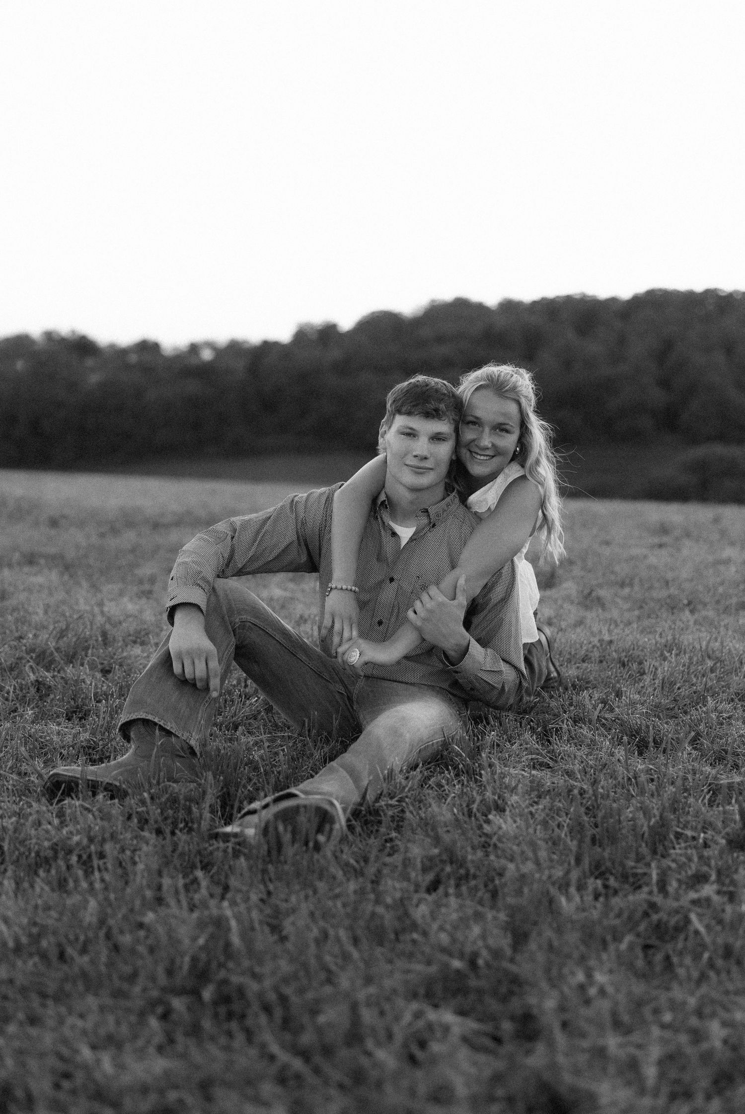 A couple lying together in a grassy meadow on a summer day, captured in black and white.