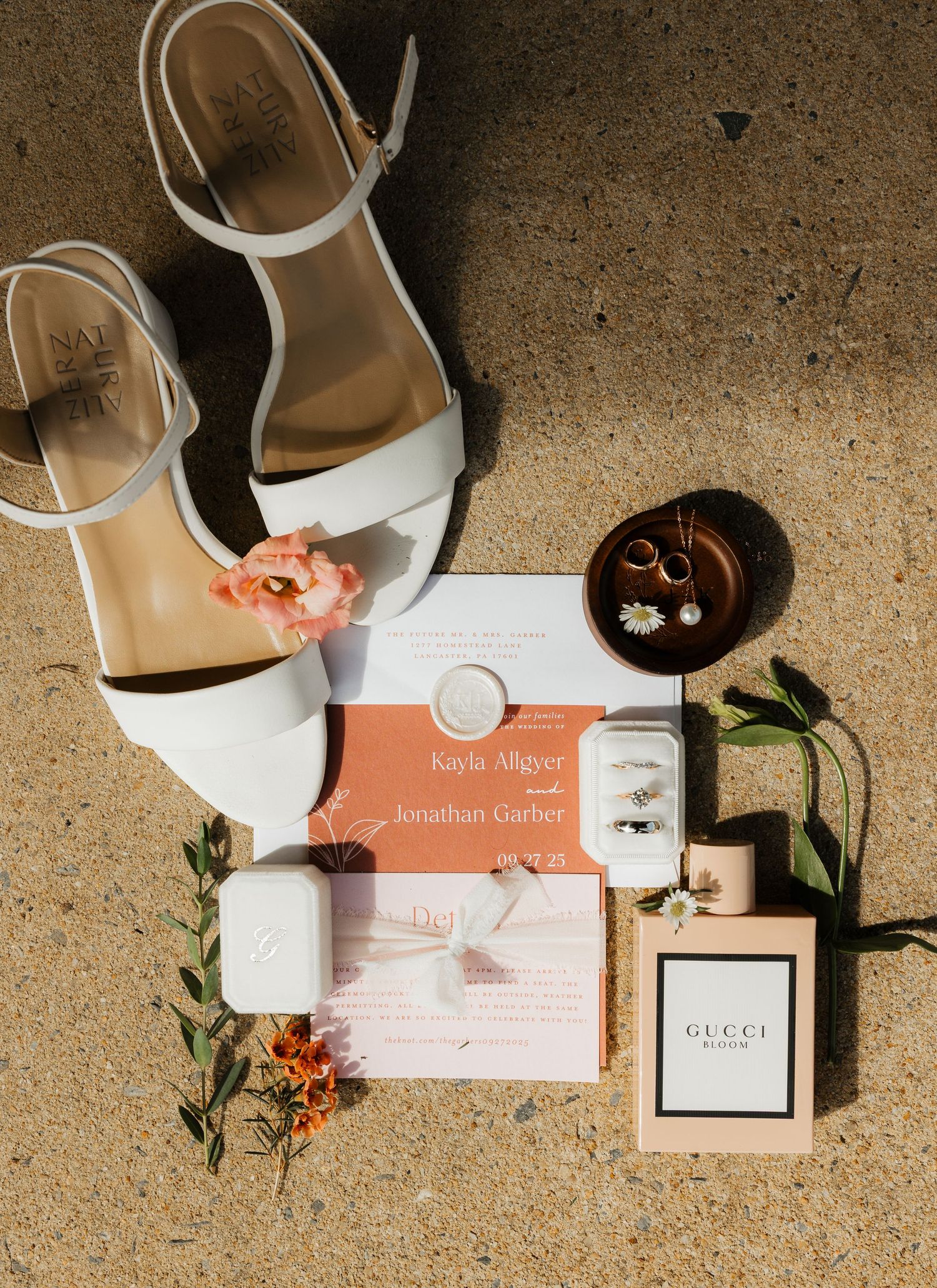 Wedding invitation cards and accessories arranged artistically on a textured beige surface with white shoes and floral elements.