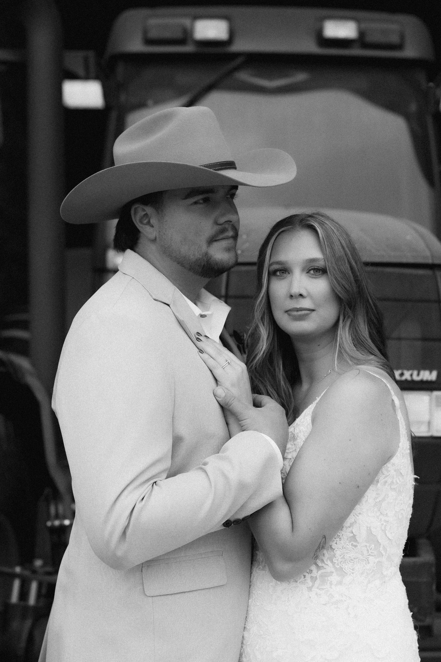 A black and white wedding photo of a couple embracing, with the groom wearing a cowboy hat and suit.