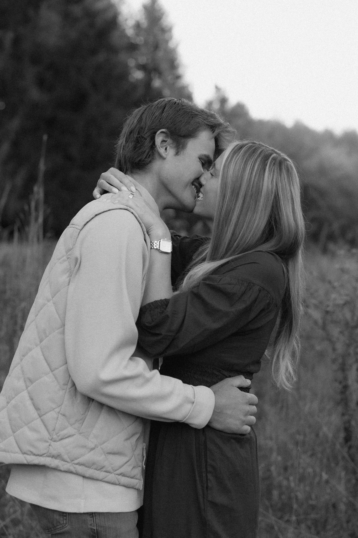 Black and white photo series showing a couple embracing in a field with tall grass and trees in the background.