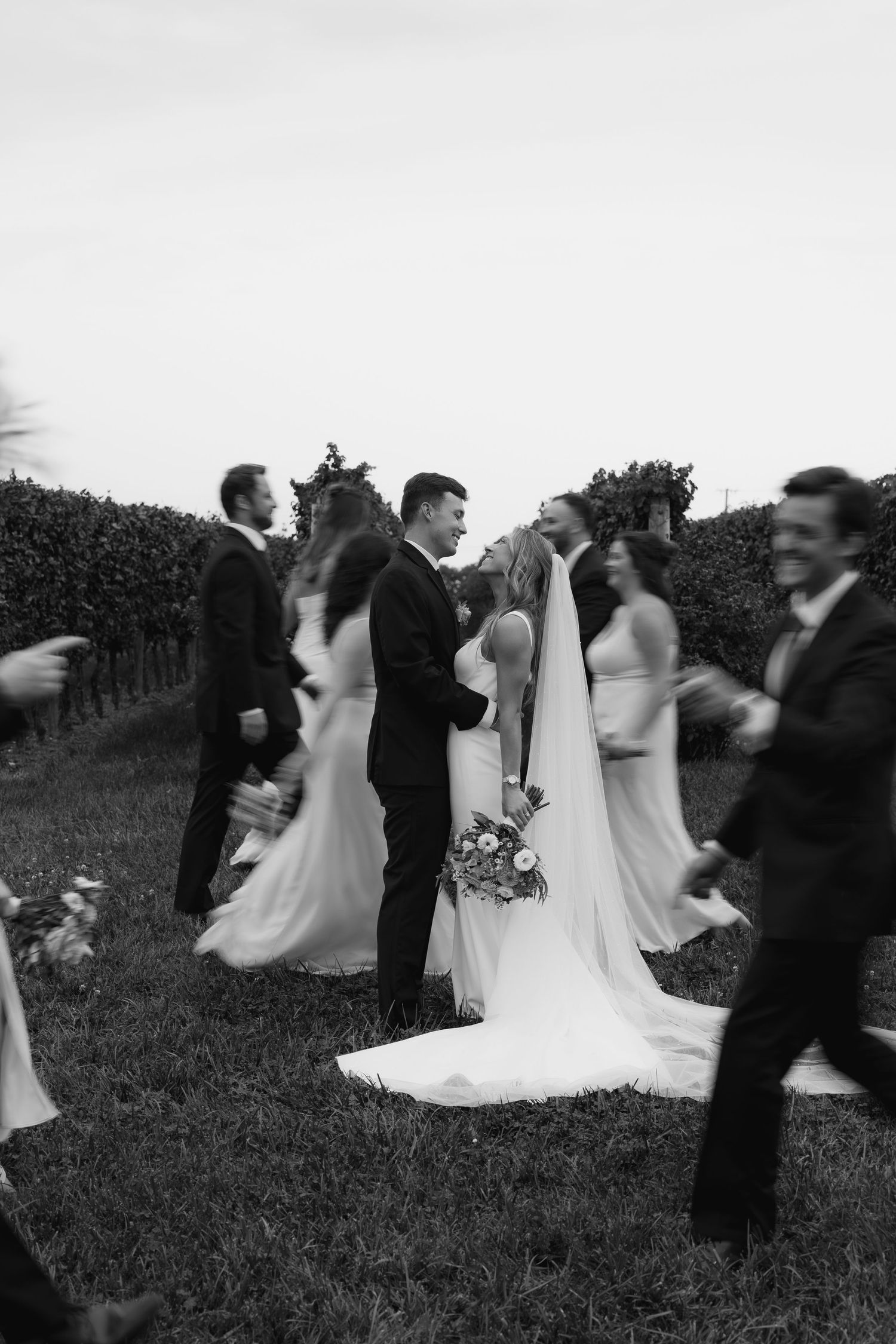Black and white sequence of wedding party dancing and spinning in a grassy outdoor setting.