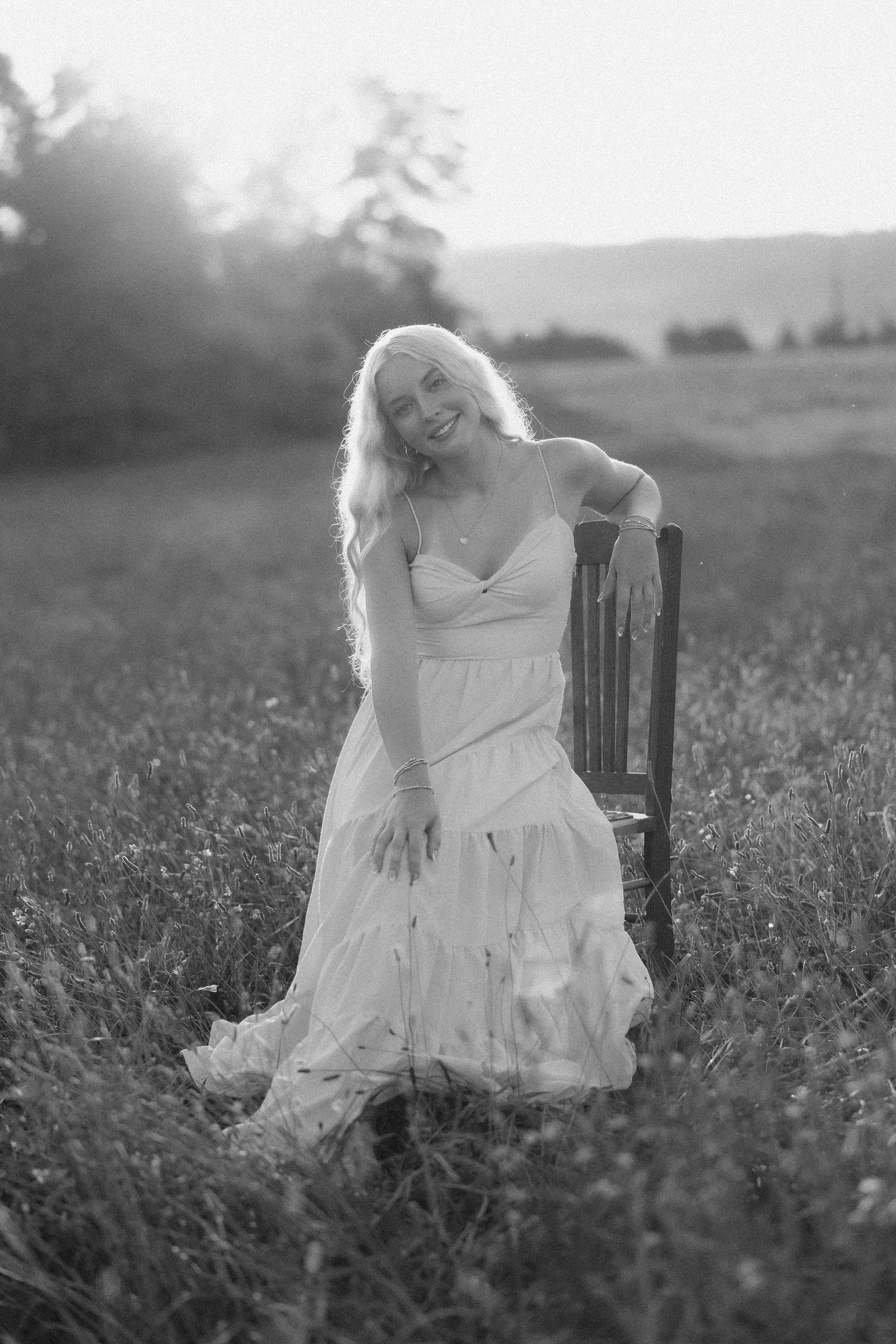 A dreamy black and white photo series shows a figure in a flowing white dress sitting in a wildflower meadow at dusk.