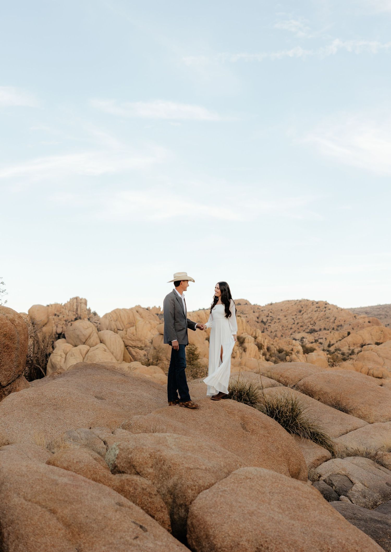 Two people walk along scenic desert rock formations at sunset in Joshua Tree National Park.
