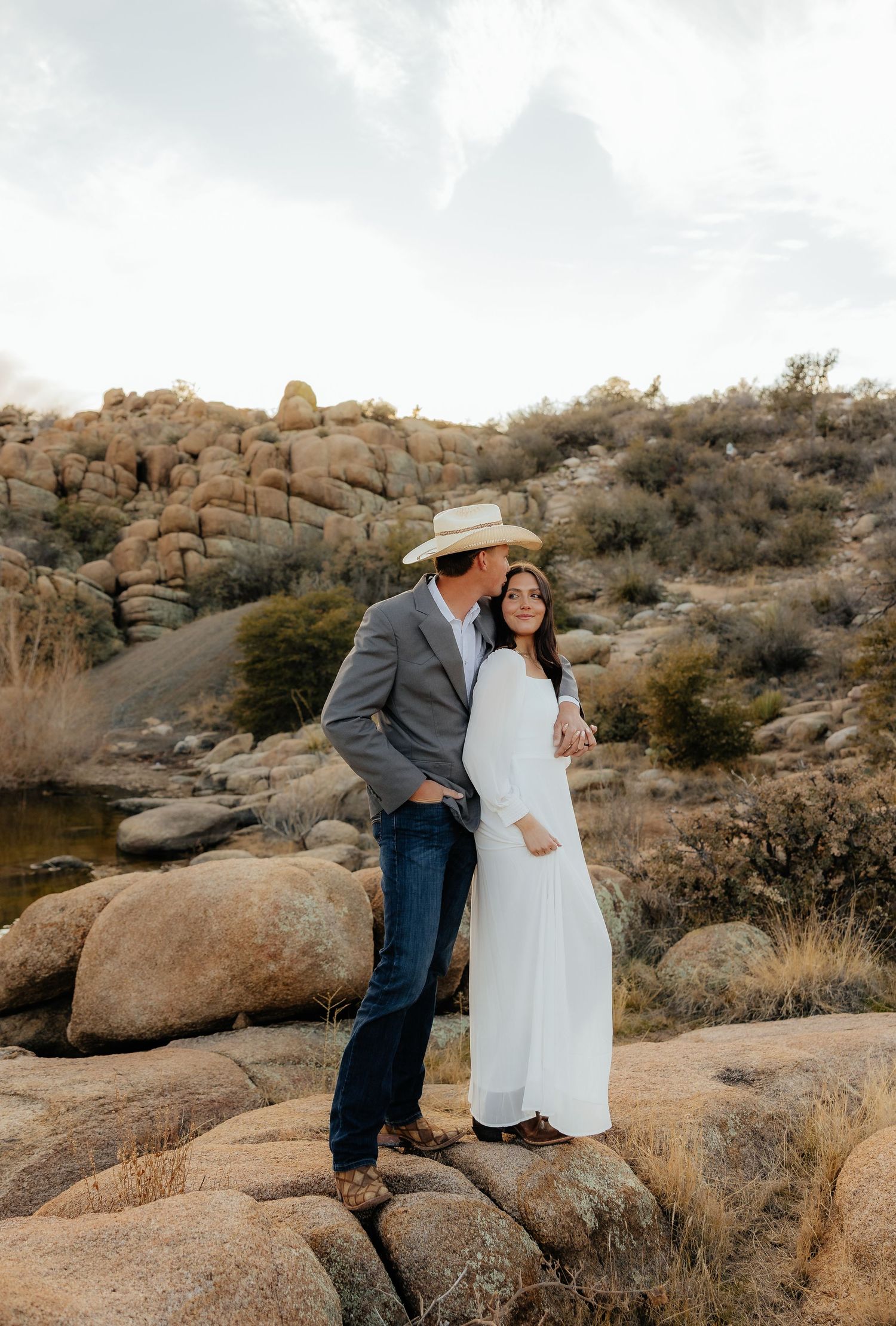 A couple in western attire shares romantic moments among desert rock formations during a rustic outdoor photo session.