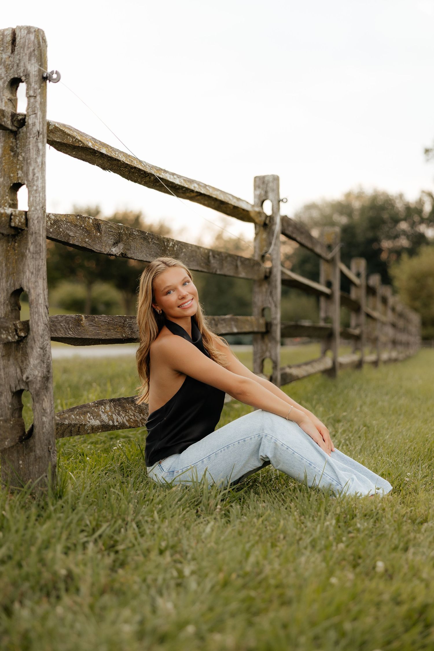 A person relaxes on green grass near a rustic wooden fence in a peaceful countryside setting.