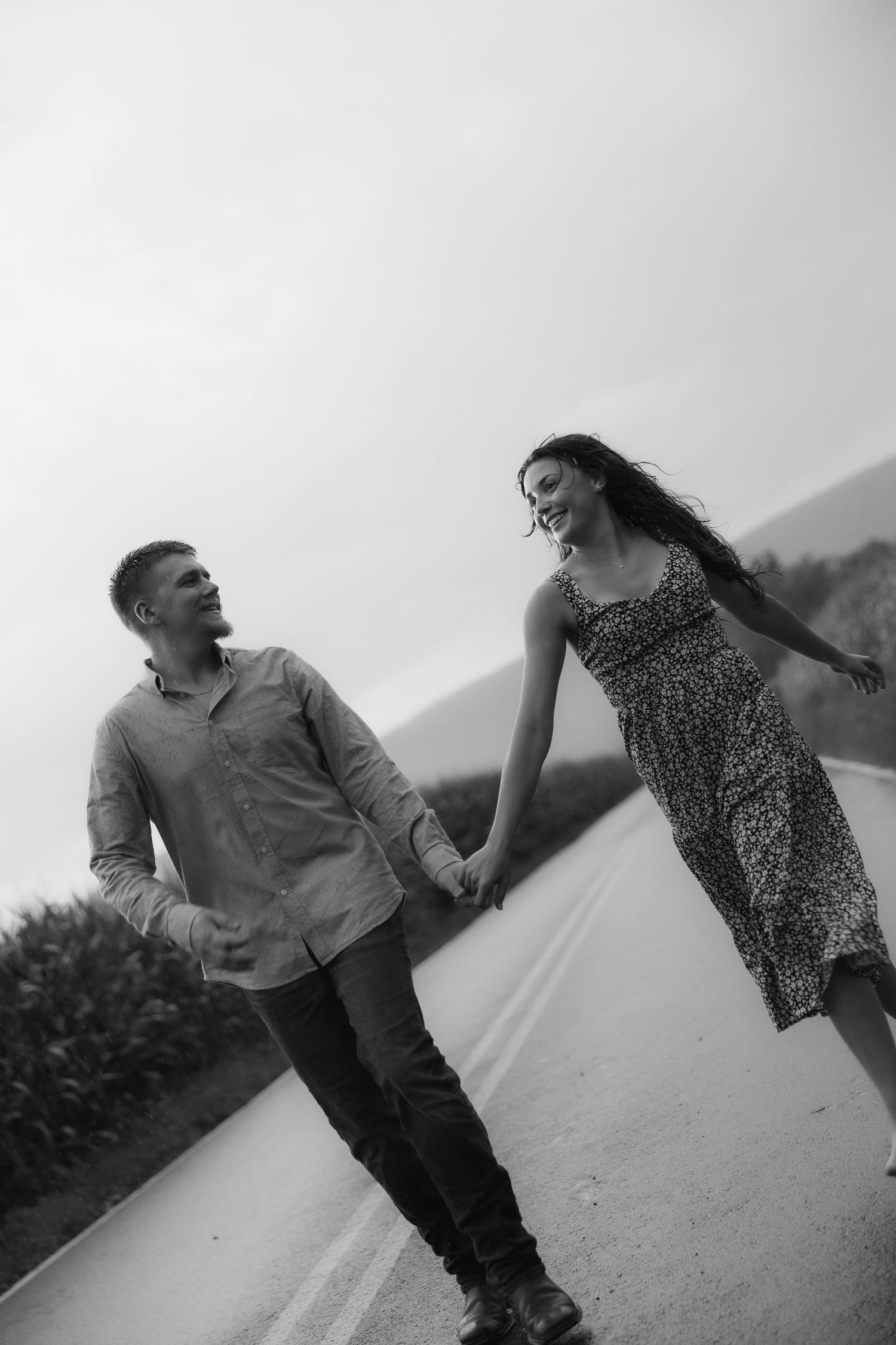 Couple playfully running and laughing together on a path in black and white.