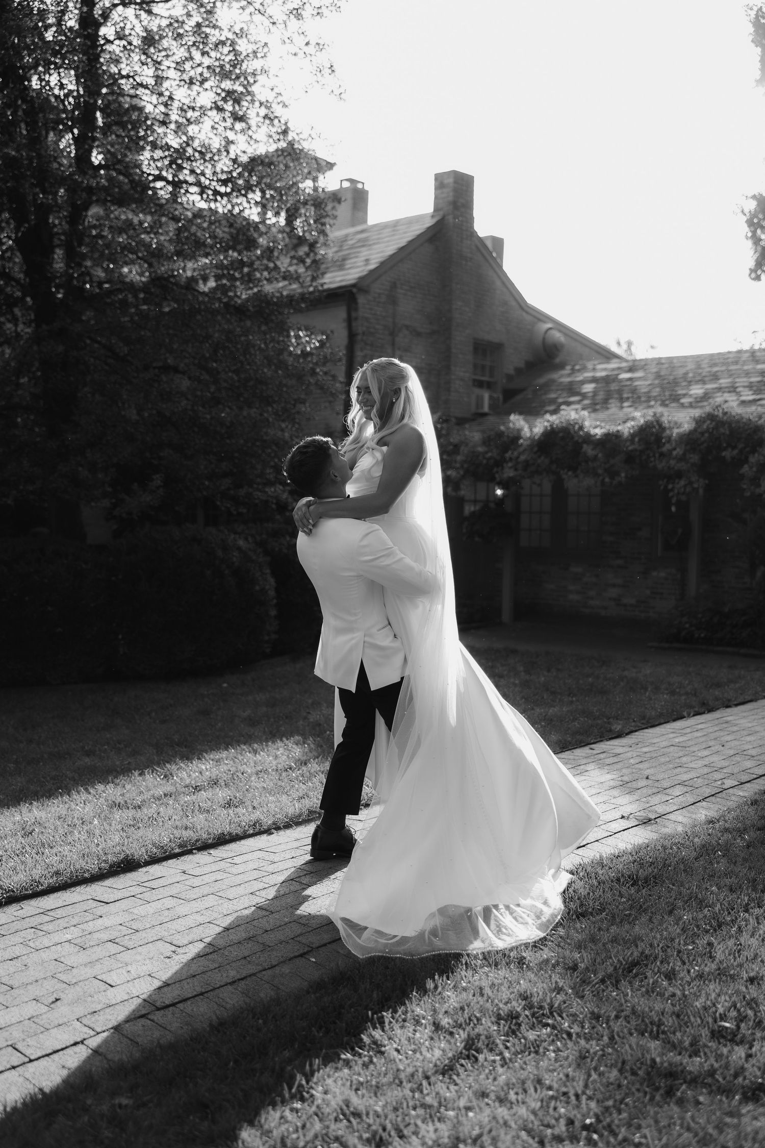 A couple in wedding attire poses on a stone pathway at sunset.