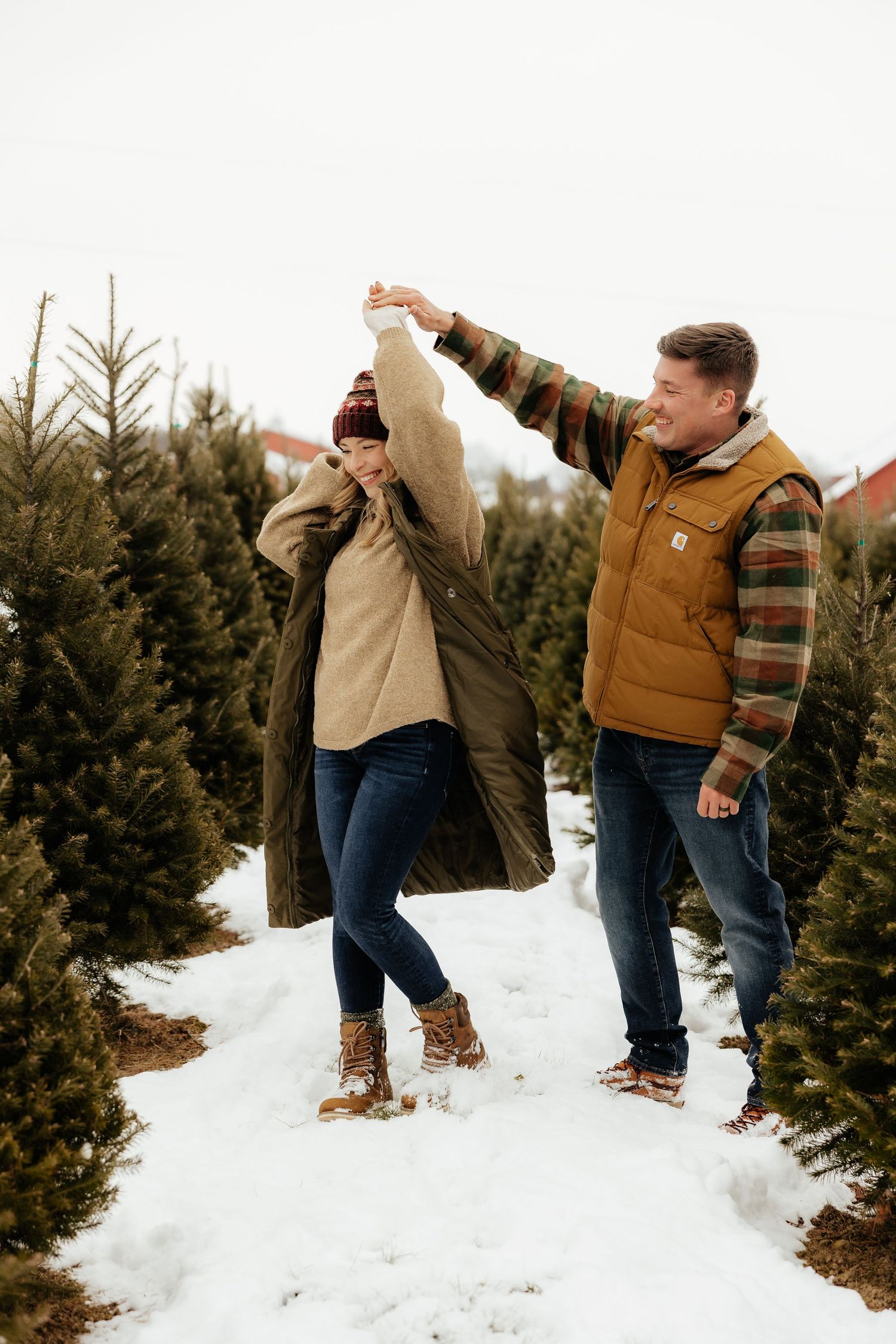 A couple playfully dances together in the snow at a Christmas tree farm on a winter day.
