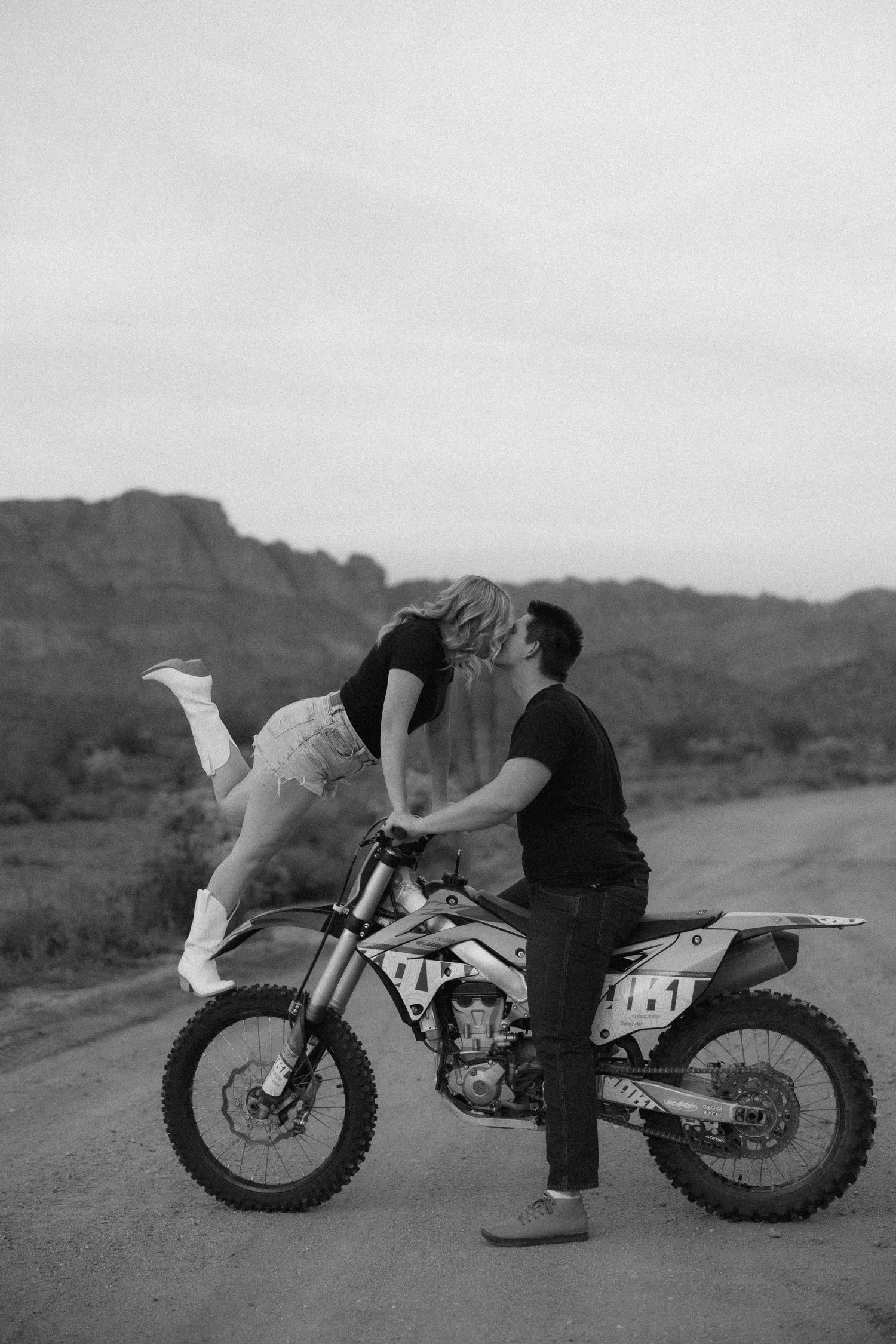 Black and white photos capture a couple's romantic poses with a dirt bike against a mountainous backdrop.
