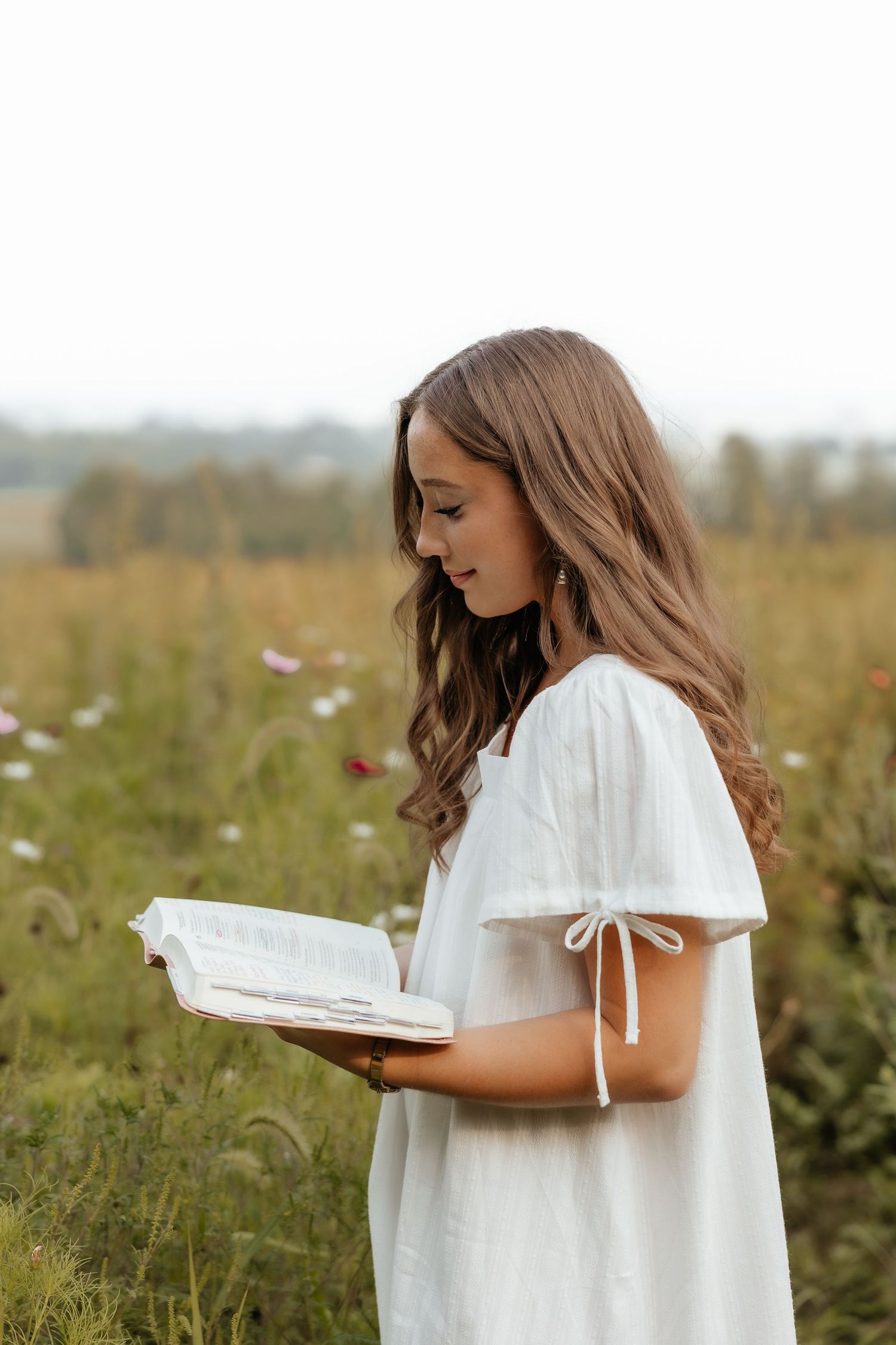 Young woman in white dress reading a book in a blooming field.
