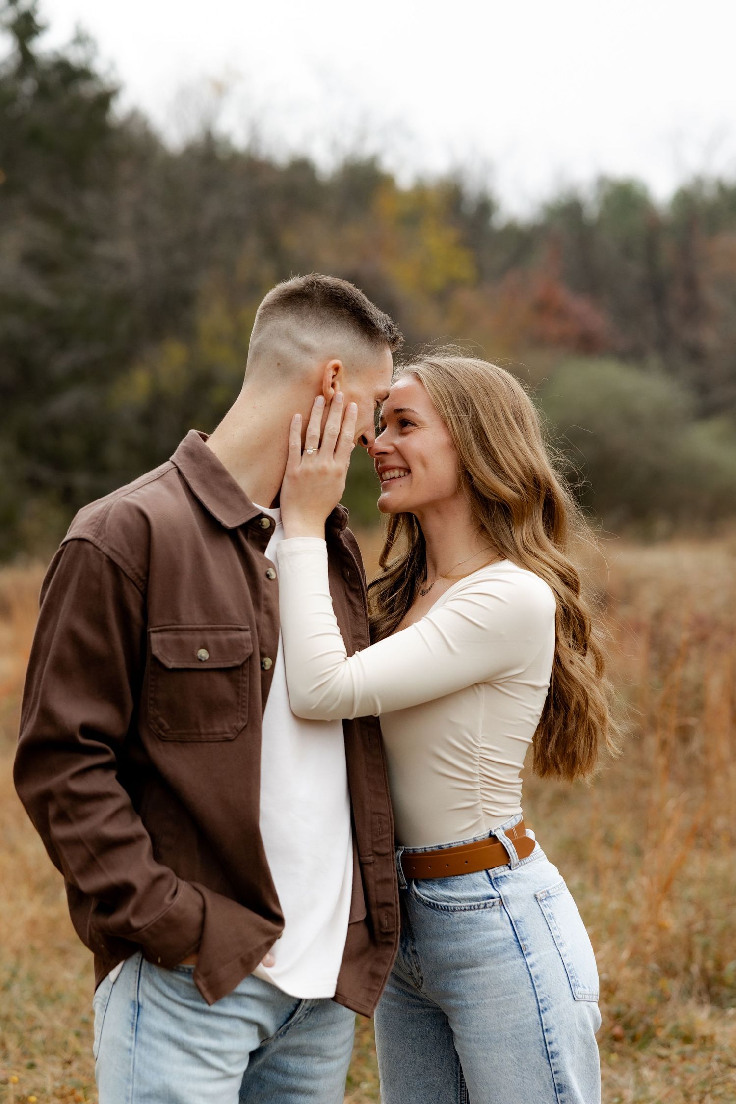 A couple in casual fall attire embraces romantically in a golden field during an autumn photoshoot.