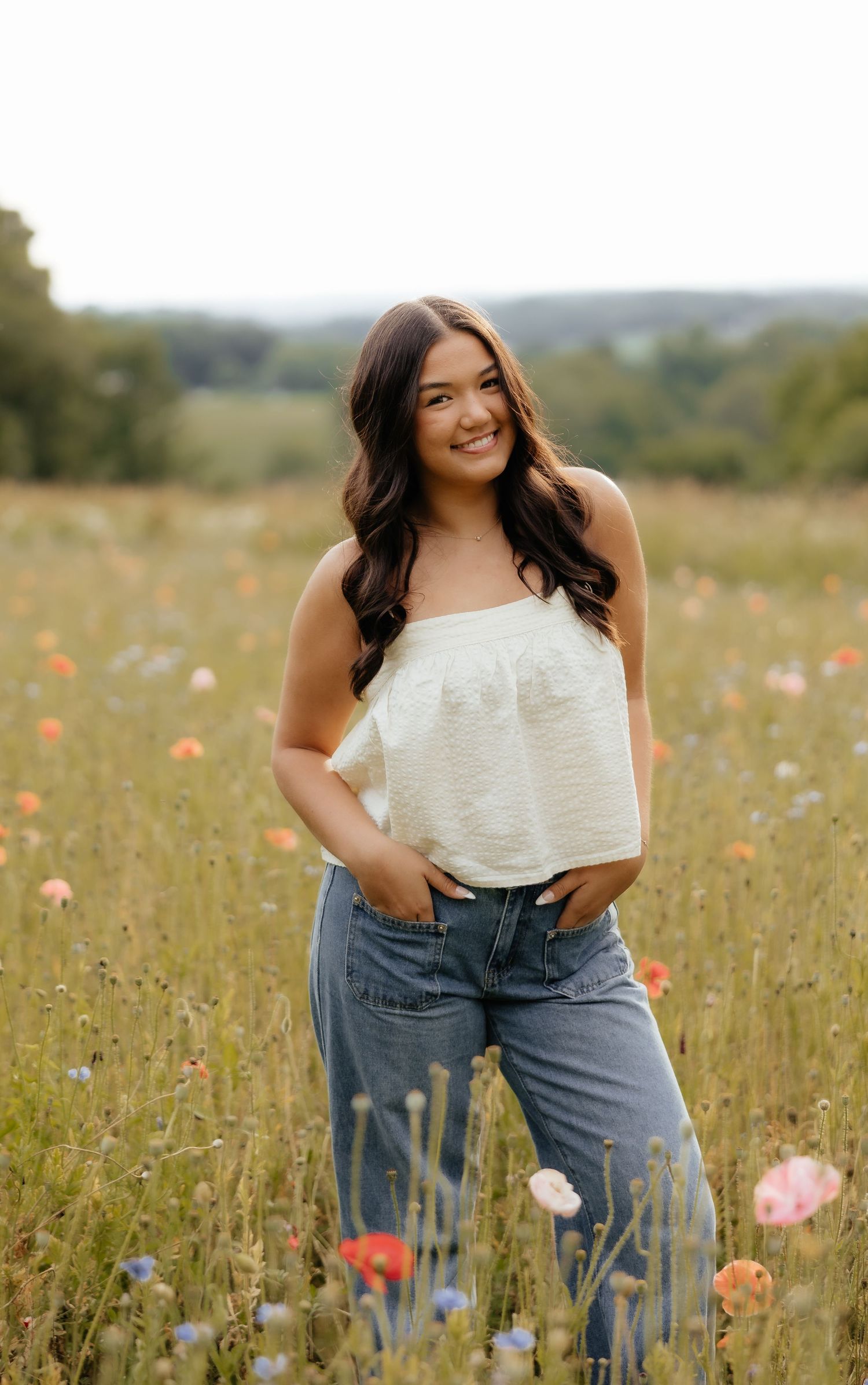 Young woman in white top and jeans smiling in a wildflower meadow on a warm summer day.