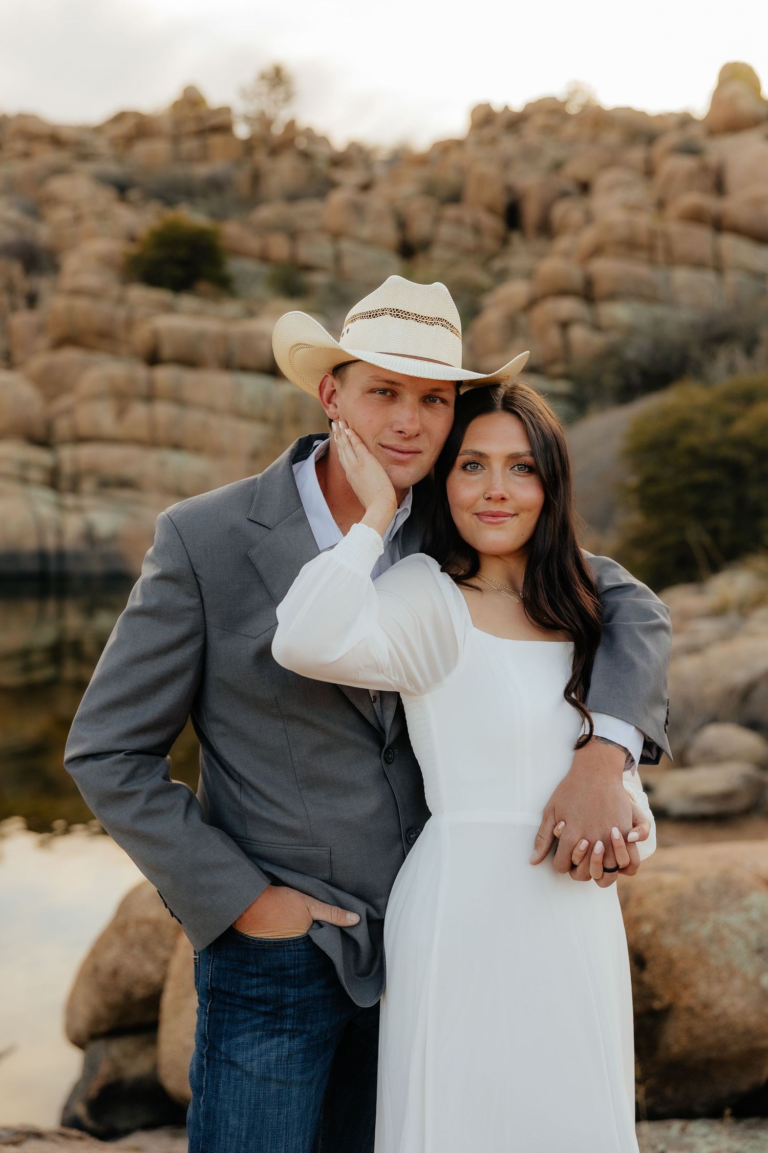 A couple poses together in front of desert rock formations during a romantic sunset photo session.