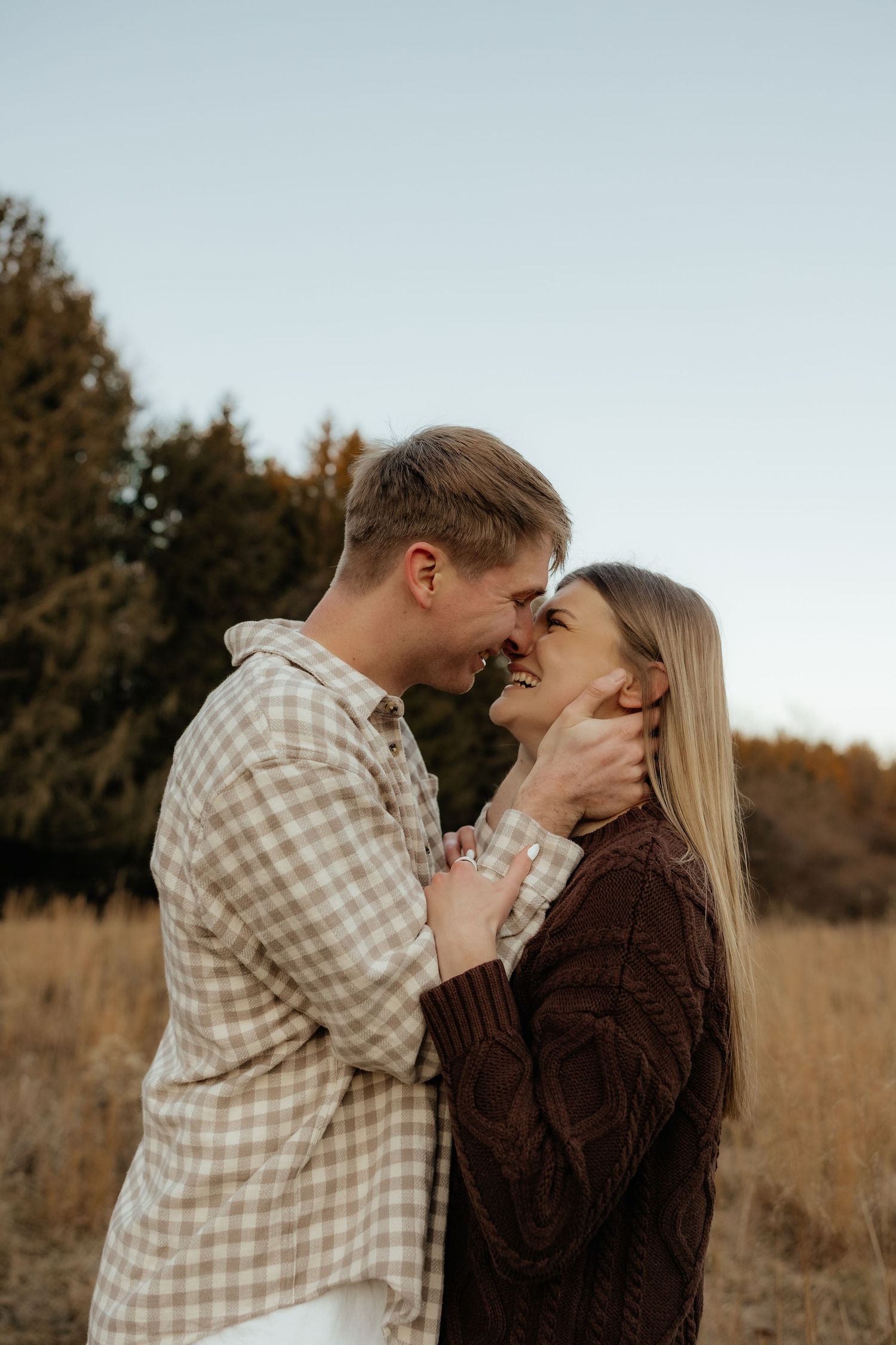 A couple shares intimate moments in a field during autumn while wearing cozy sweaters.
