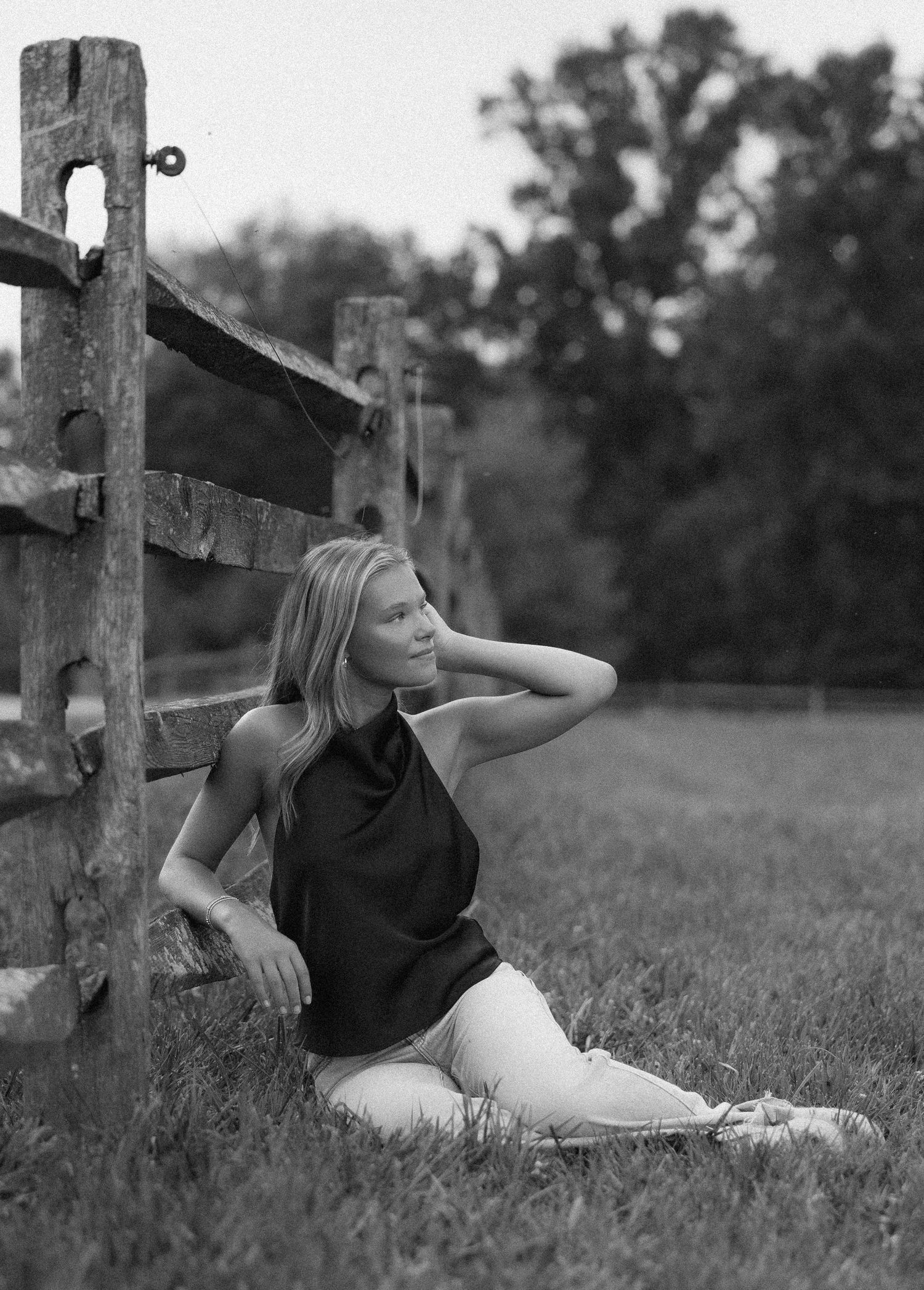Black and white artistic portrait series showing person reclining against rustic wooden fence in outdoor field setting.